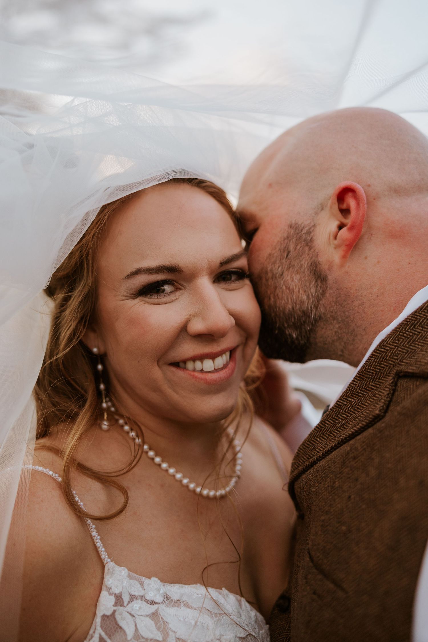 Close-up wedding portrait with veil and pearl necklace details.