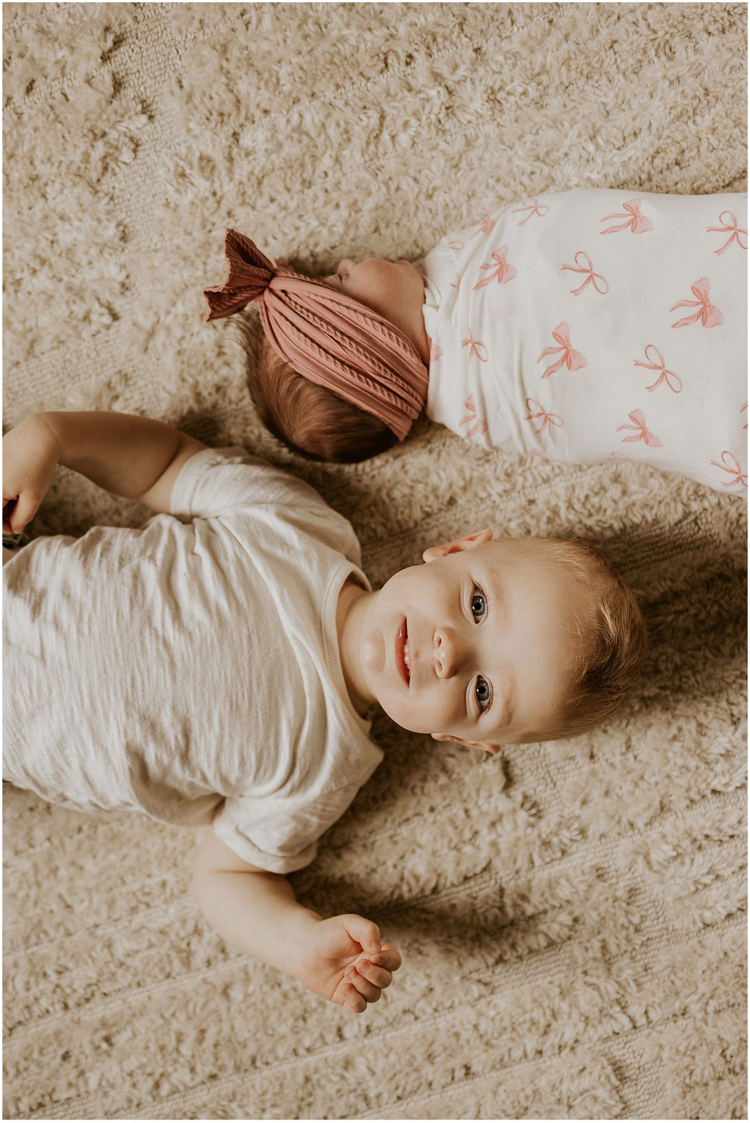 Toddler laying next to his newborn baby sister