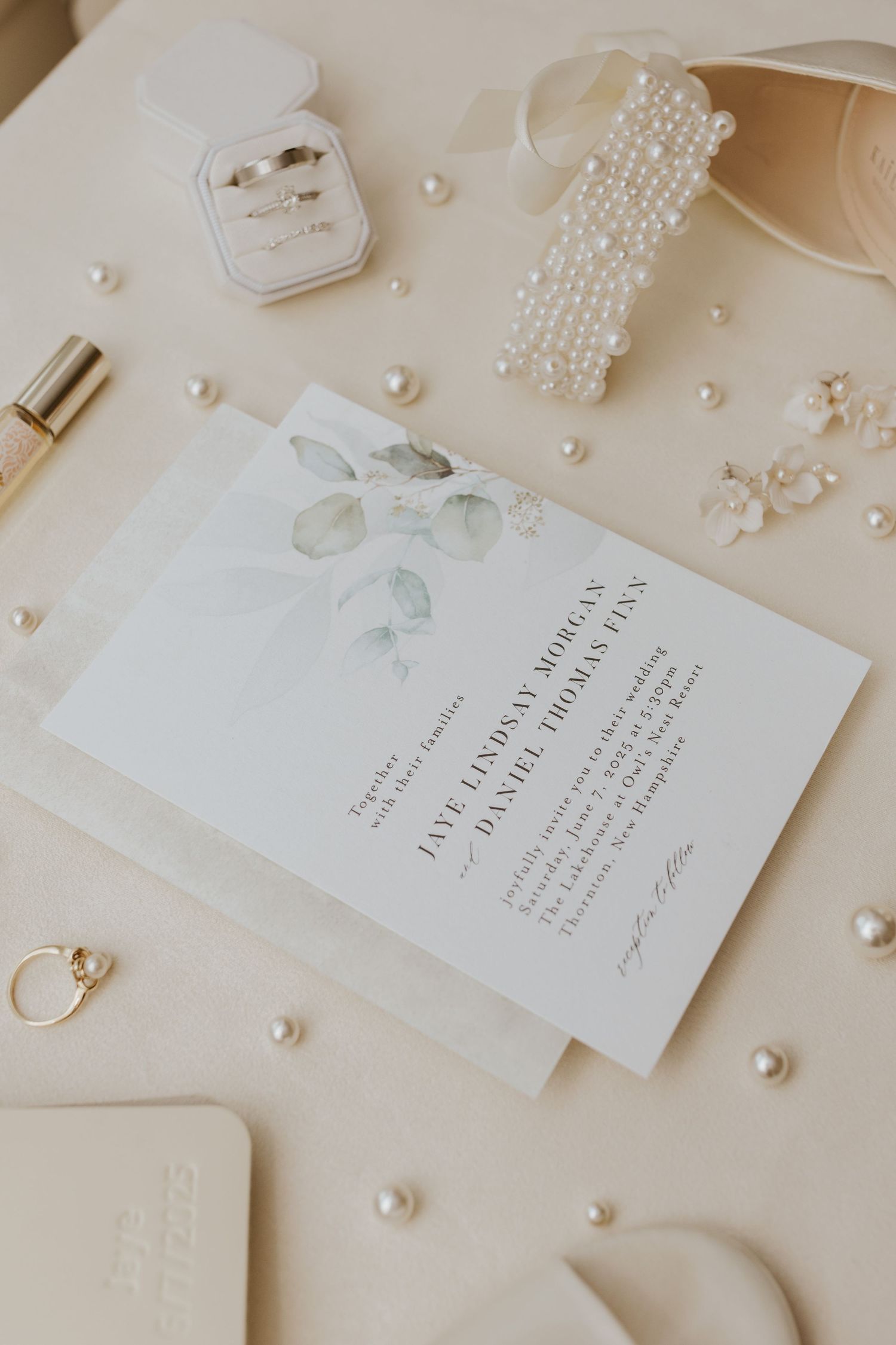 Wedding invitation suite flatlay with rings, pearls, and floral stationery on a cream background.