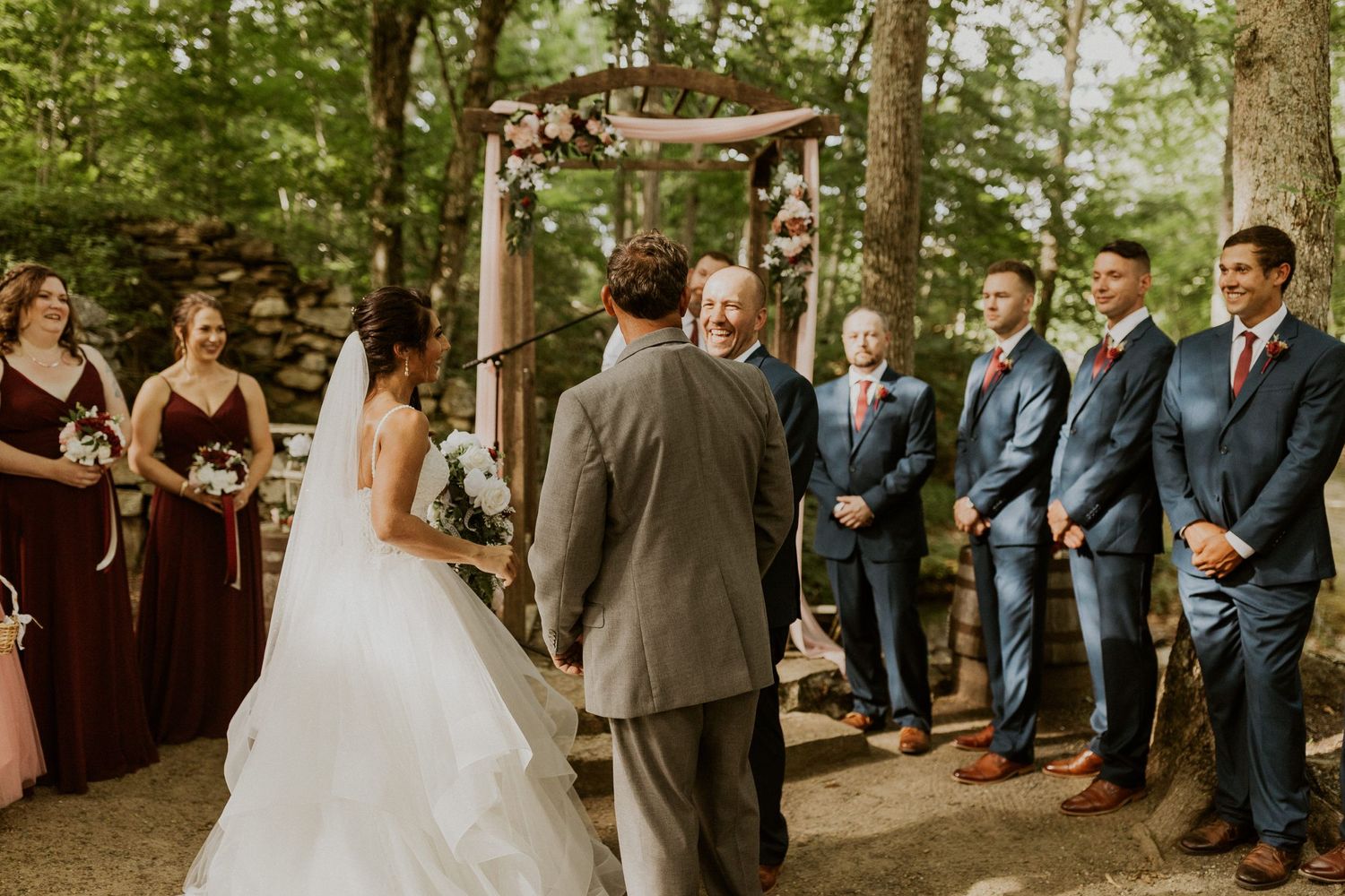 Wedding ceremony taking place in a natural woodland setting with rustic wooden seating.