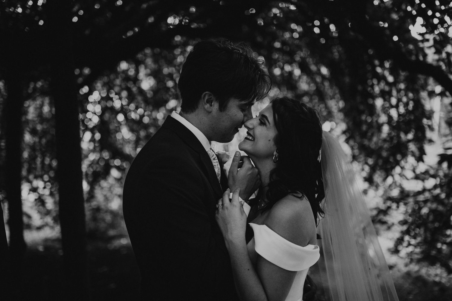 Romantic outdoor wedding moment captured under lush tree canopy.