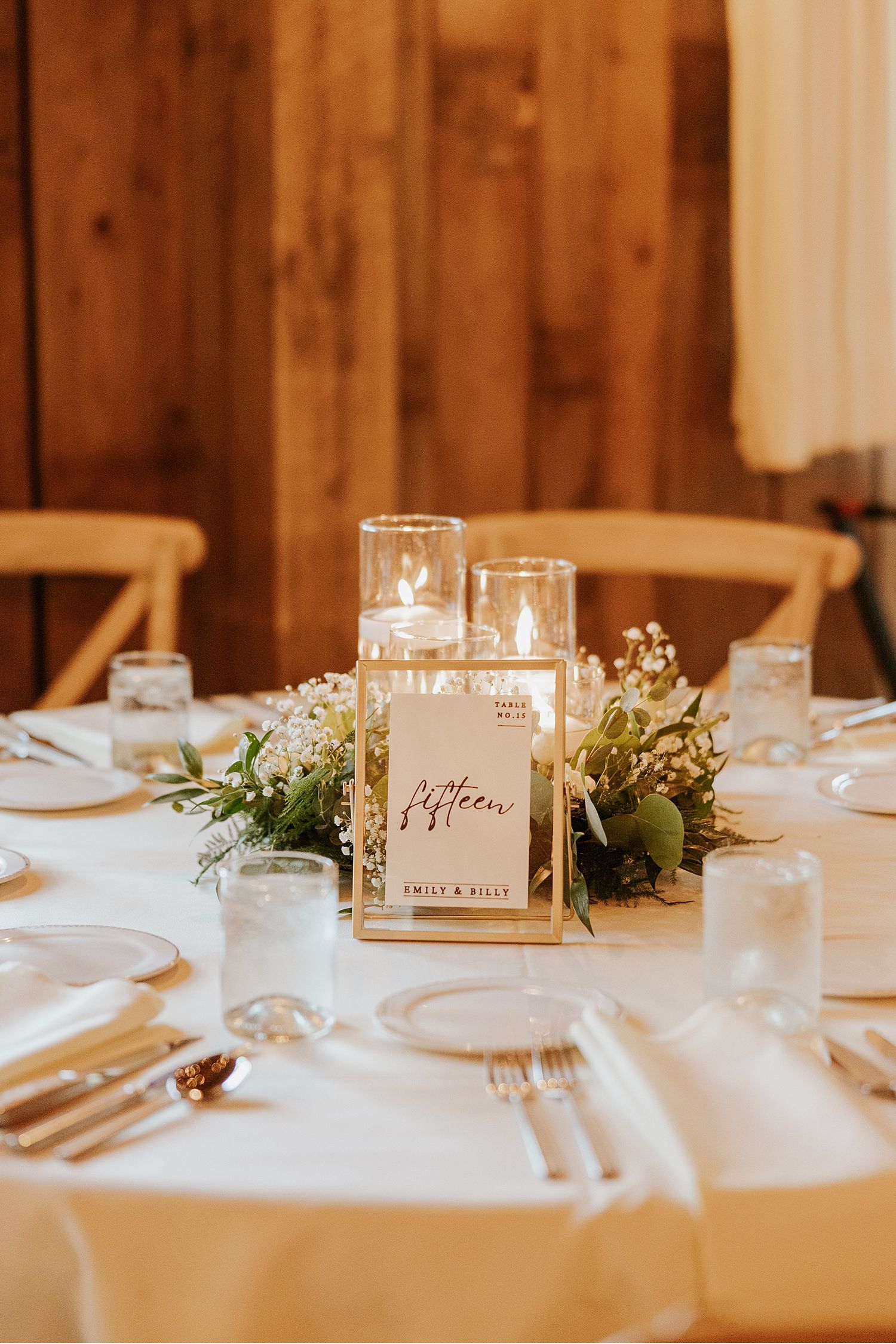 Elegant wedding reception table setting with white linens, candles and greenery decorations.