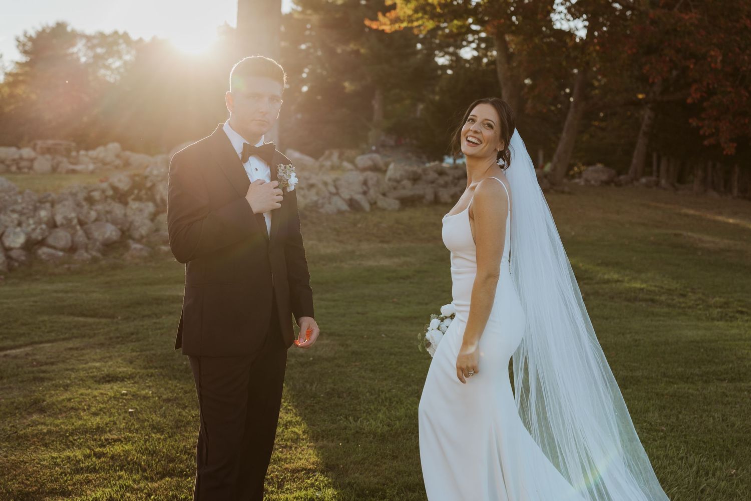 Bride laughs joyfully beside groom at golden hour on a lush green lawn.