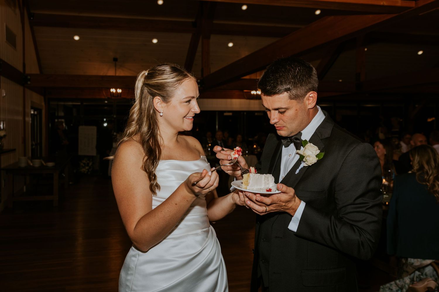 Bride and groom share a smile while cutting wedding cake at their reception.
