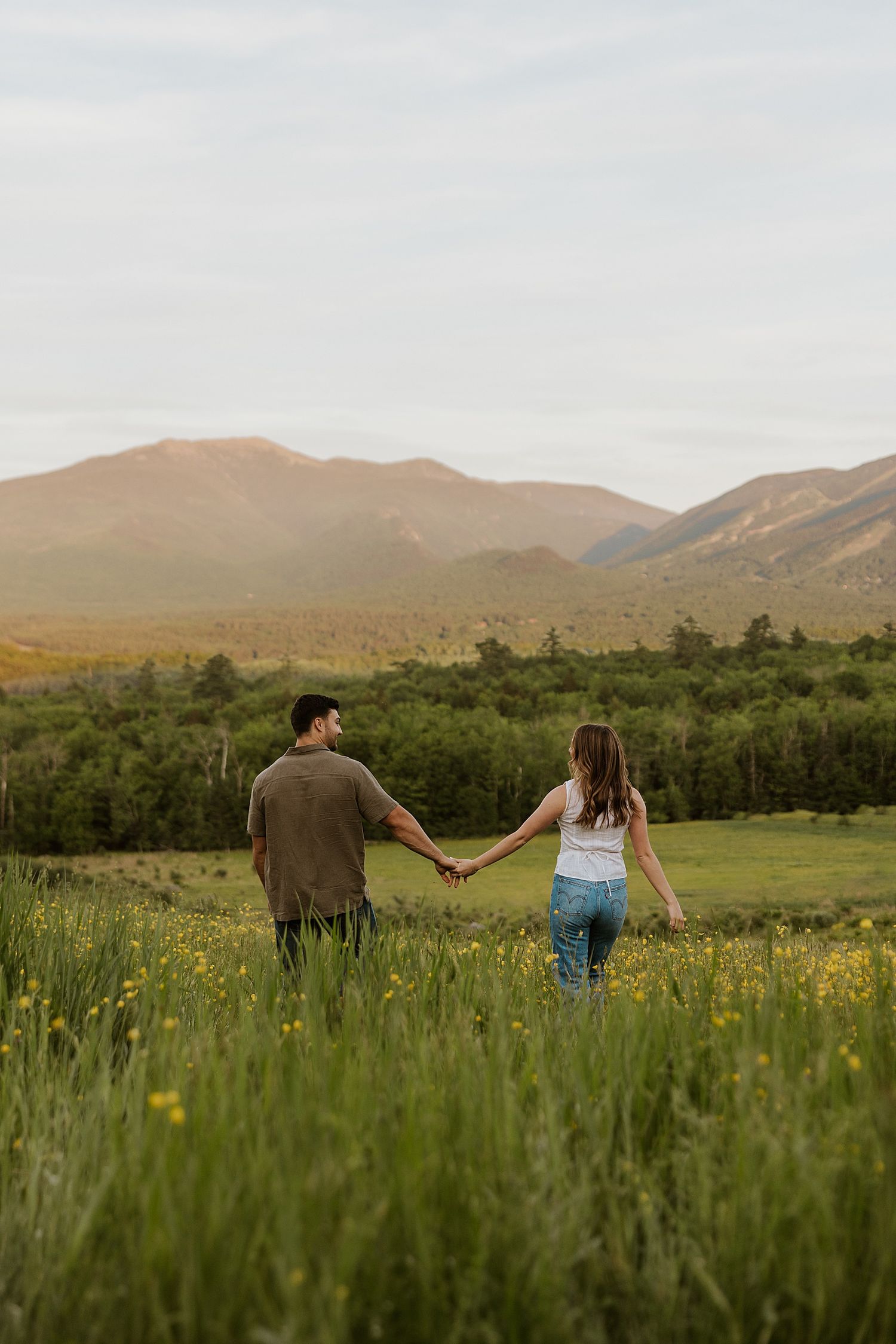 New Hampshire couple taking golden hour engagement photos in a field with the White Mountains as a backdrop