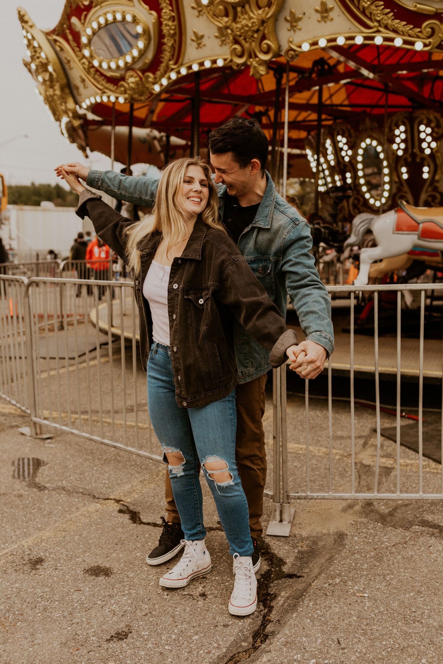 Playful couple posing together in front of a classic carnival carousel.