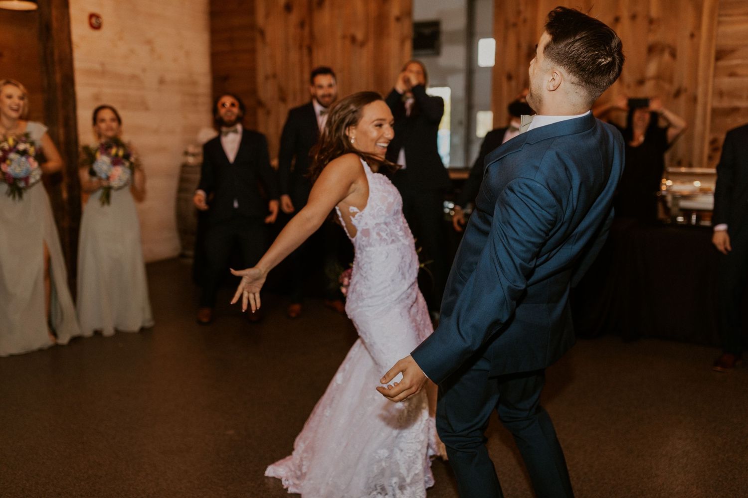 Newlyweds share a romantic dance at their rustic barn wedding reception with guests watching in the background.