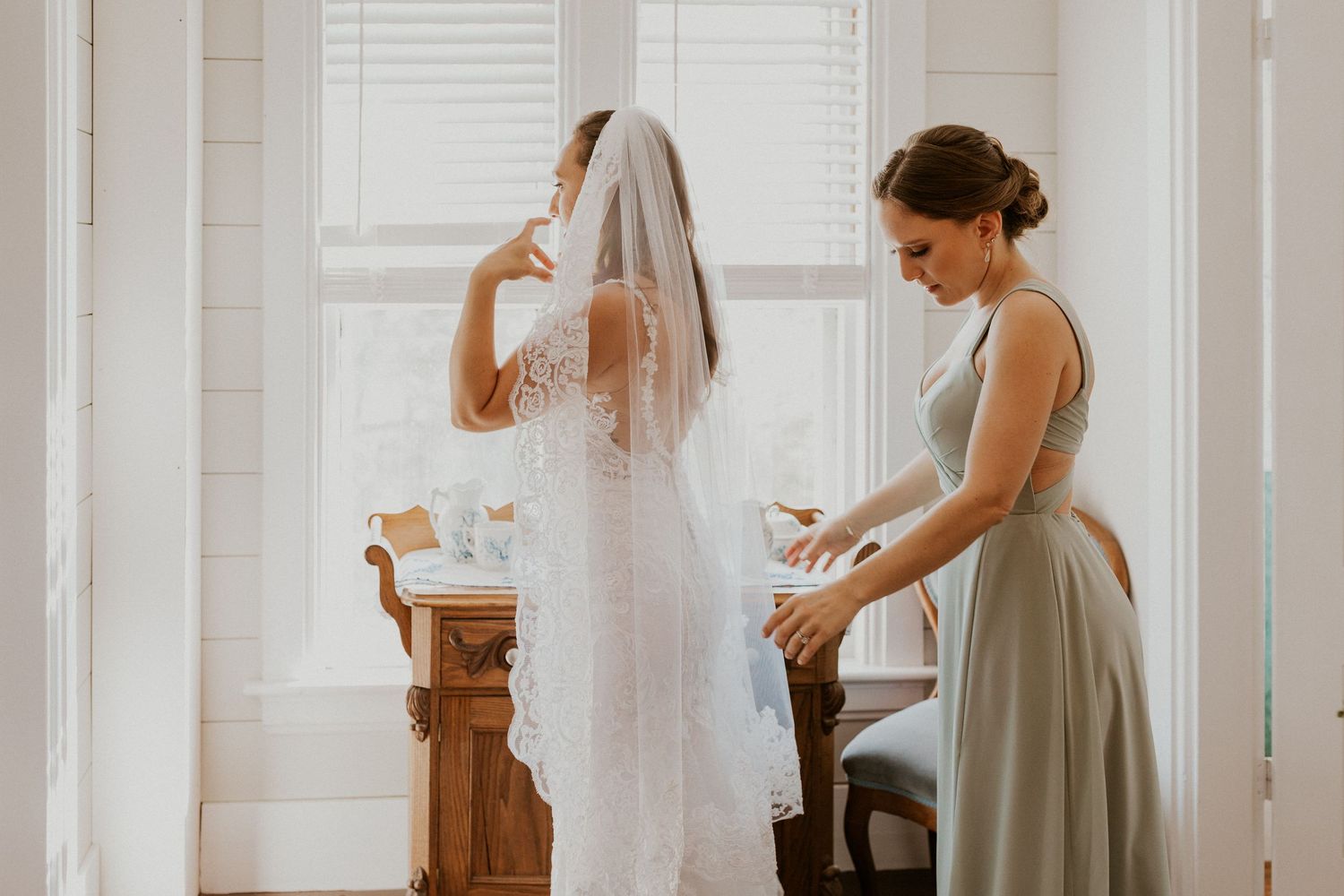 Sister of the bride helping her button her dress.