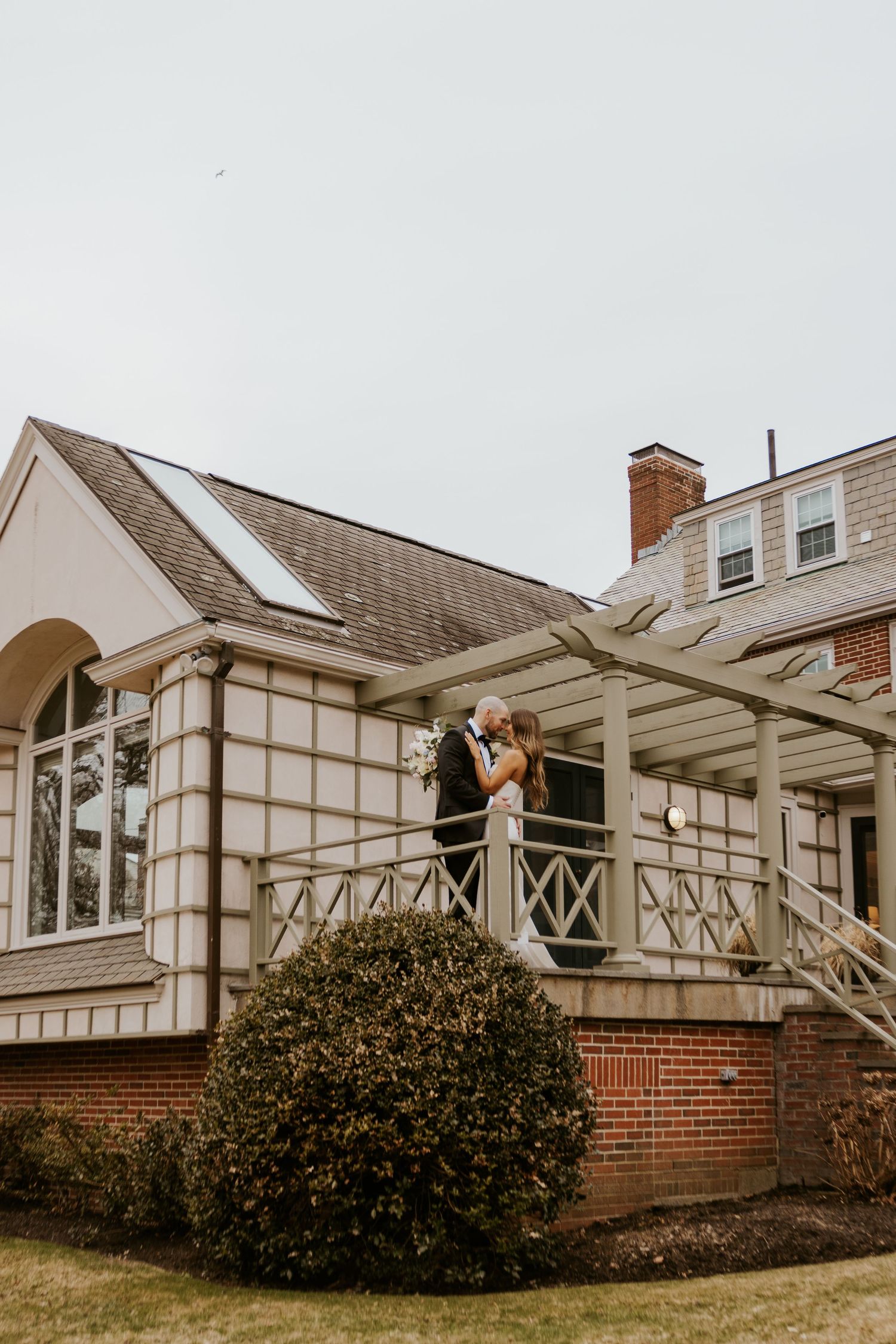 Exterior view of a brick house with Tudor-style architecture and large windows under an overcast sky.