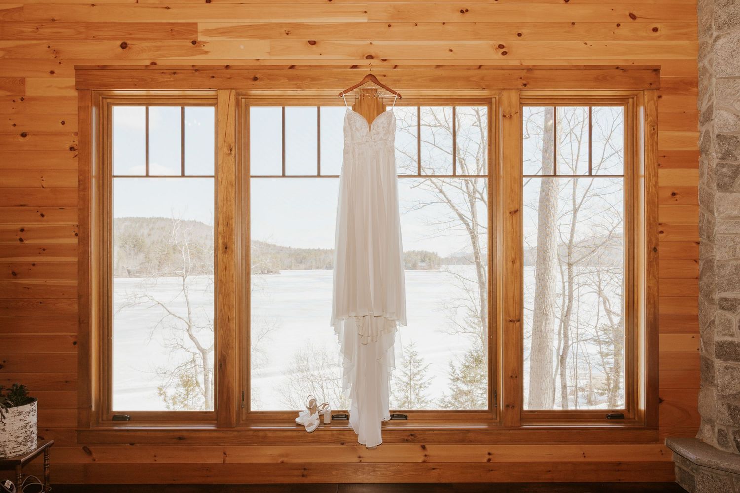 A rustic log cabin interior features exposed wood walls, large windows, and natural light streaming in.