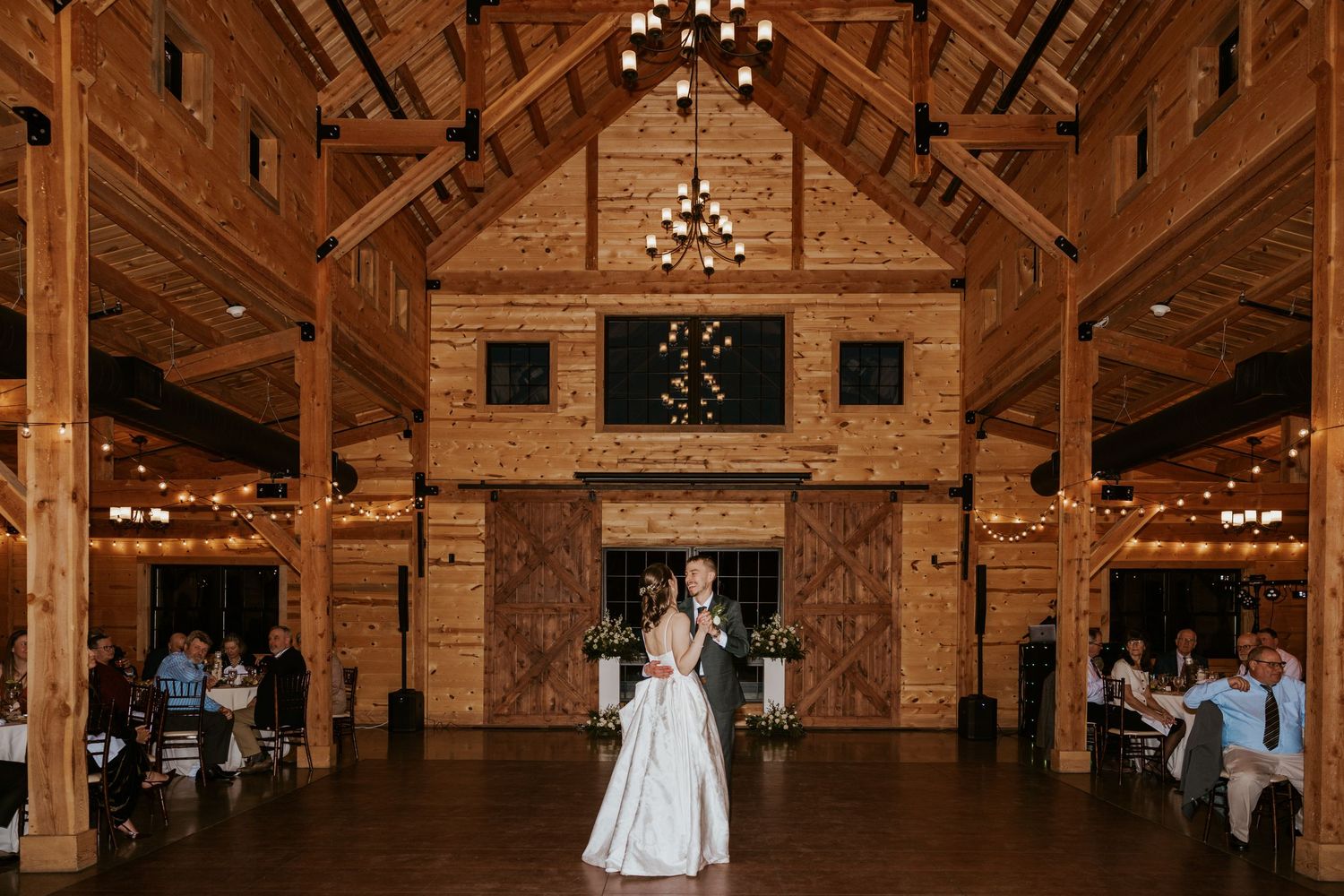 Rustic wooden barn venue decorated with elegant chandeliers and string lights for an evening wedding reception.