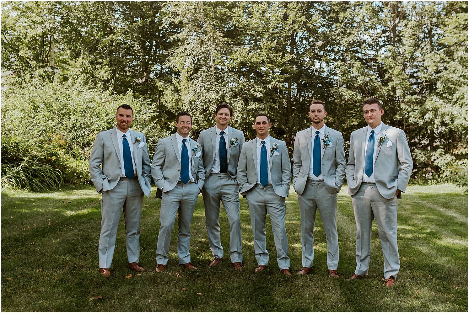 Groomsmen in light blue suits and matching ties lined up outdoors for wedding photos.