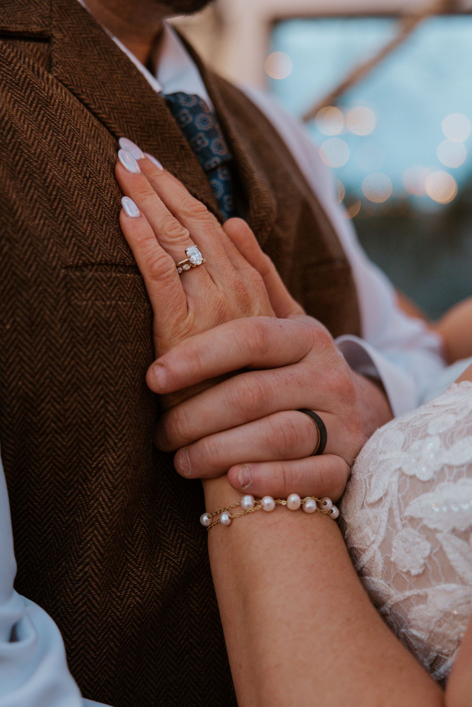 Close-up of hands wearing wedding rings and a pearl bracelet against a textured fabric background.