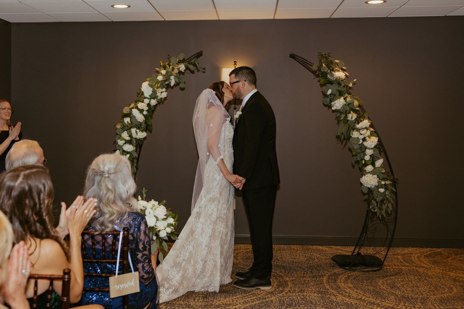 Intimate indoor wedding ceremony with floral arch decorations and soft lighting in a modern venue.