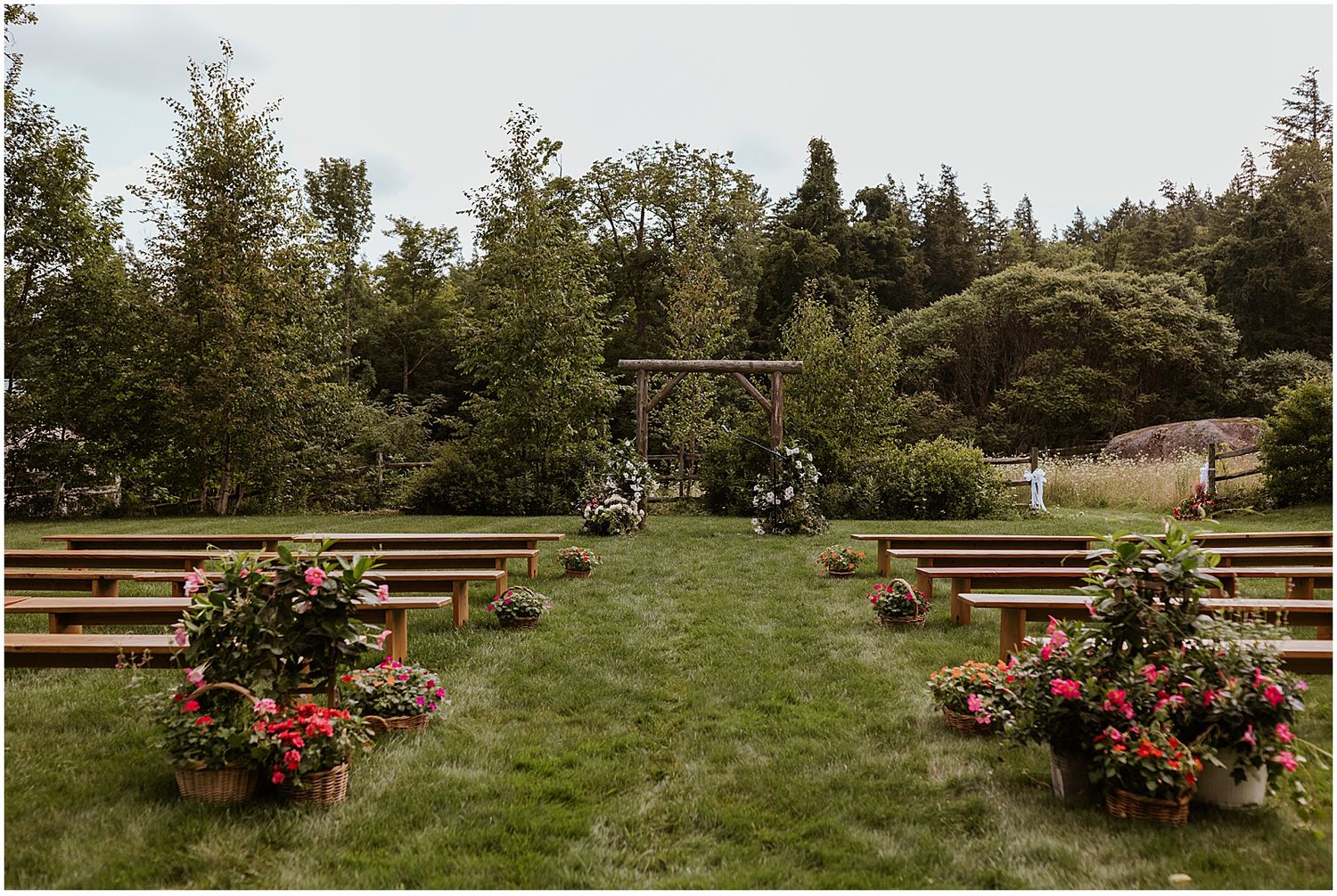 Outdoor ceremony space with wooden benches and colorful floral arrangements in a garden setting.