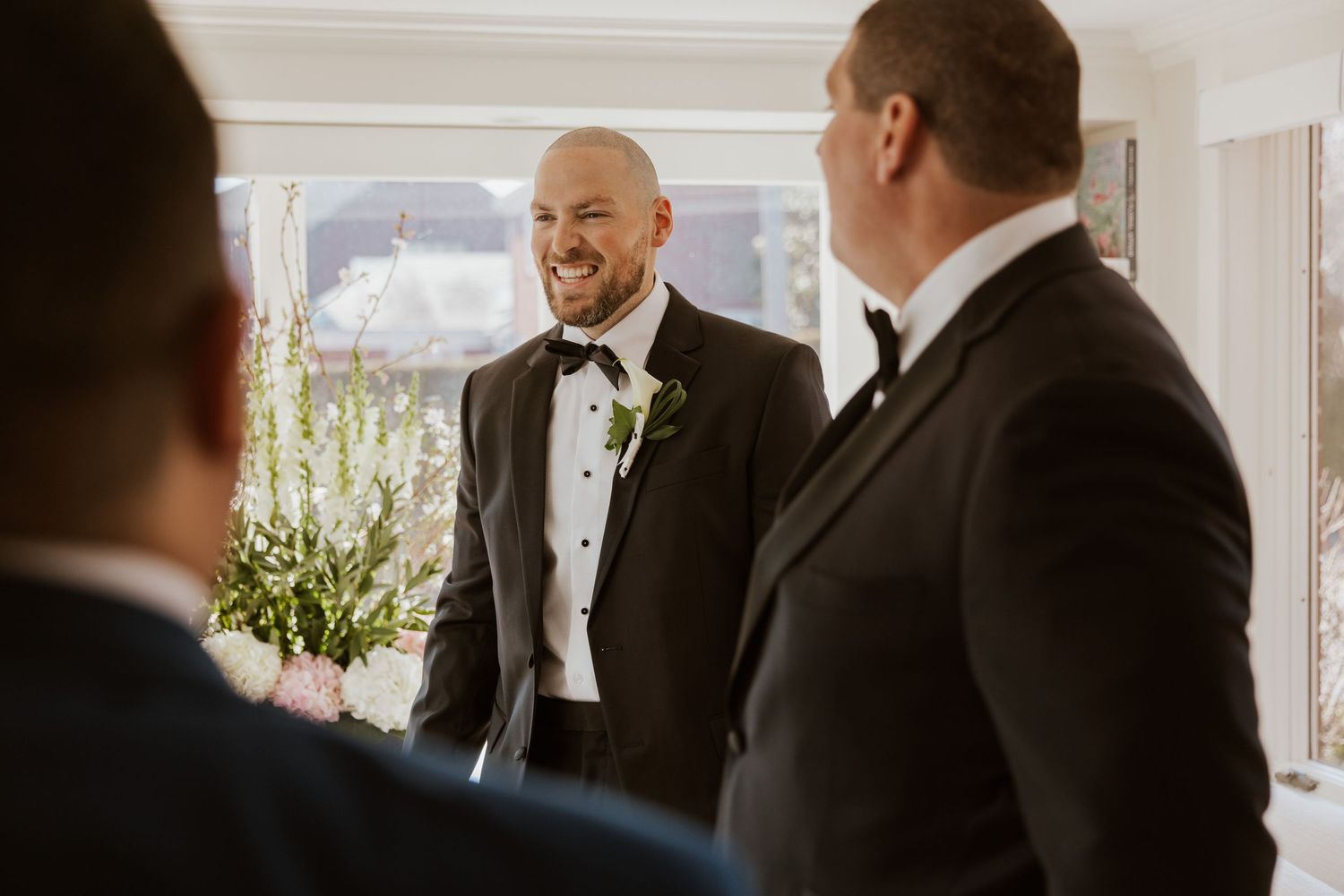 A group of people in formal attire gather and laugh together at an elegant indoor venue during a social event.
