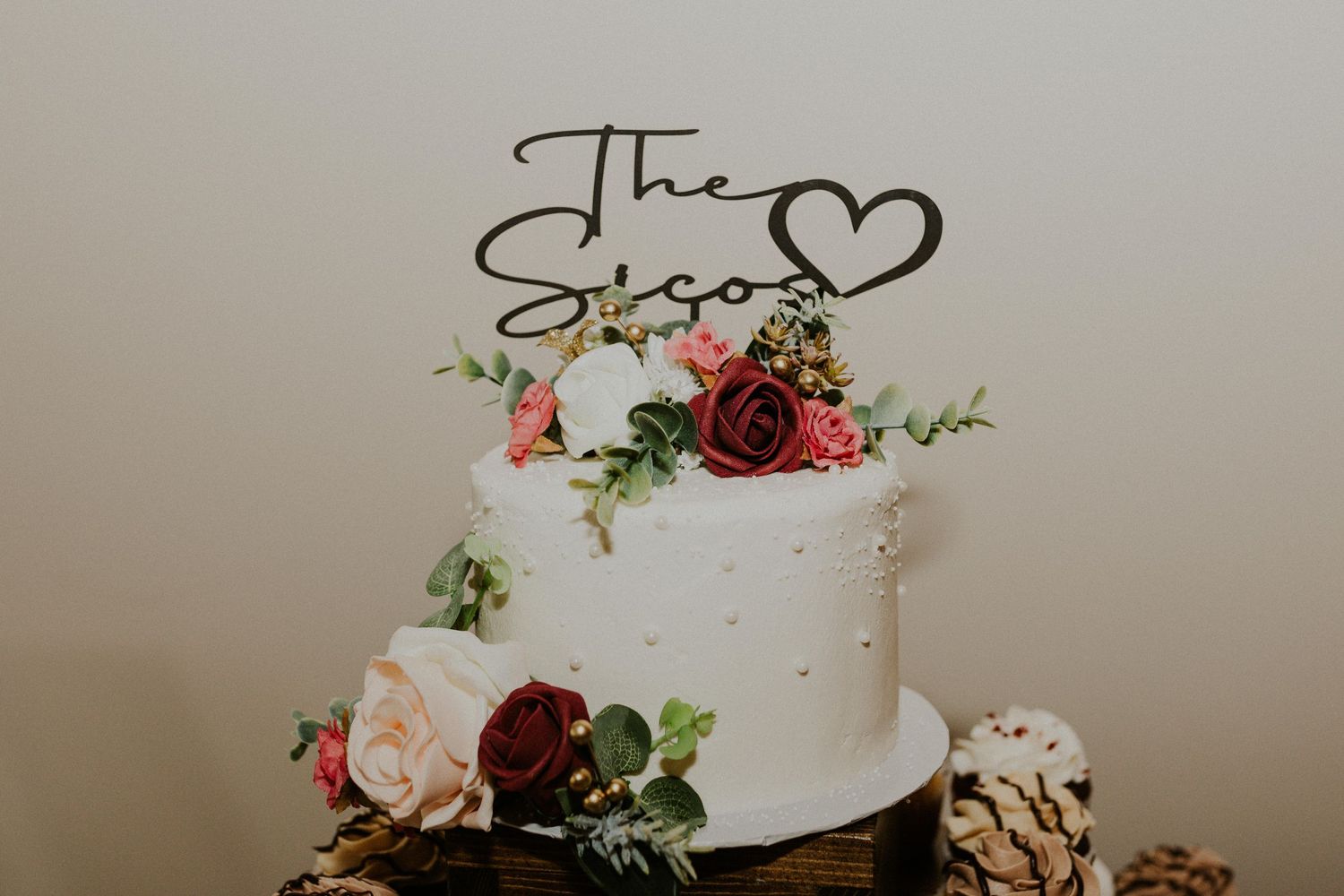 Elegant white wedding cake decorated with burgundy flowers and gold accents.