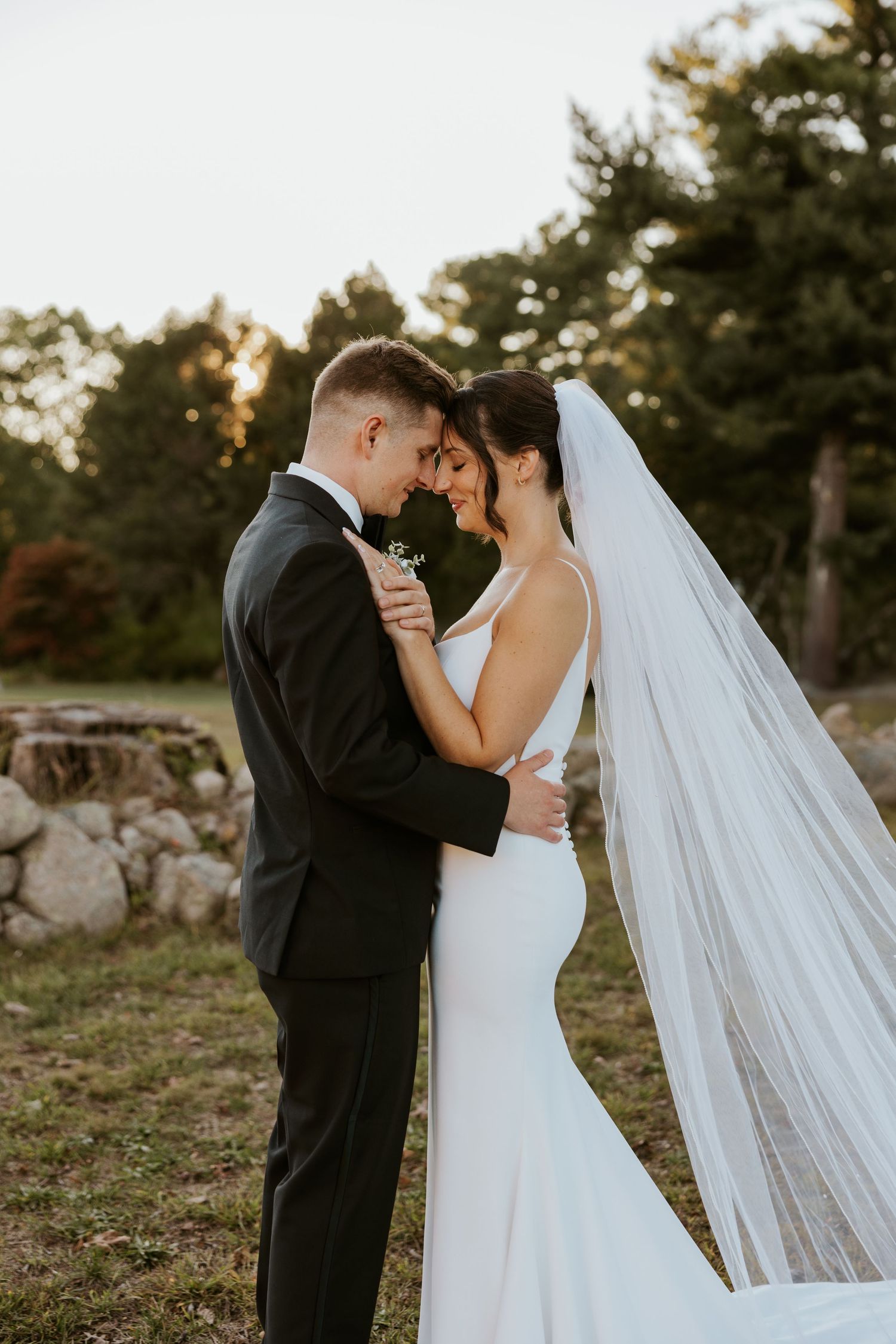 Bride and groom embrace forehead to forehead in a romantic sunset portrait outdoors.