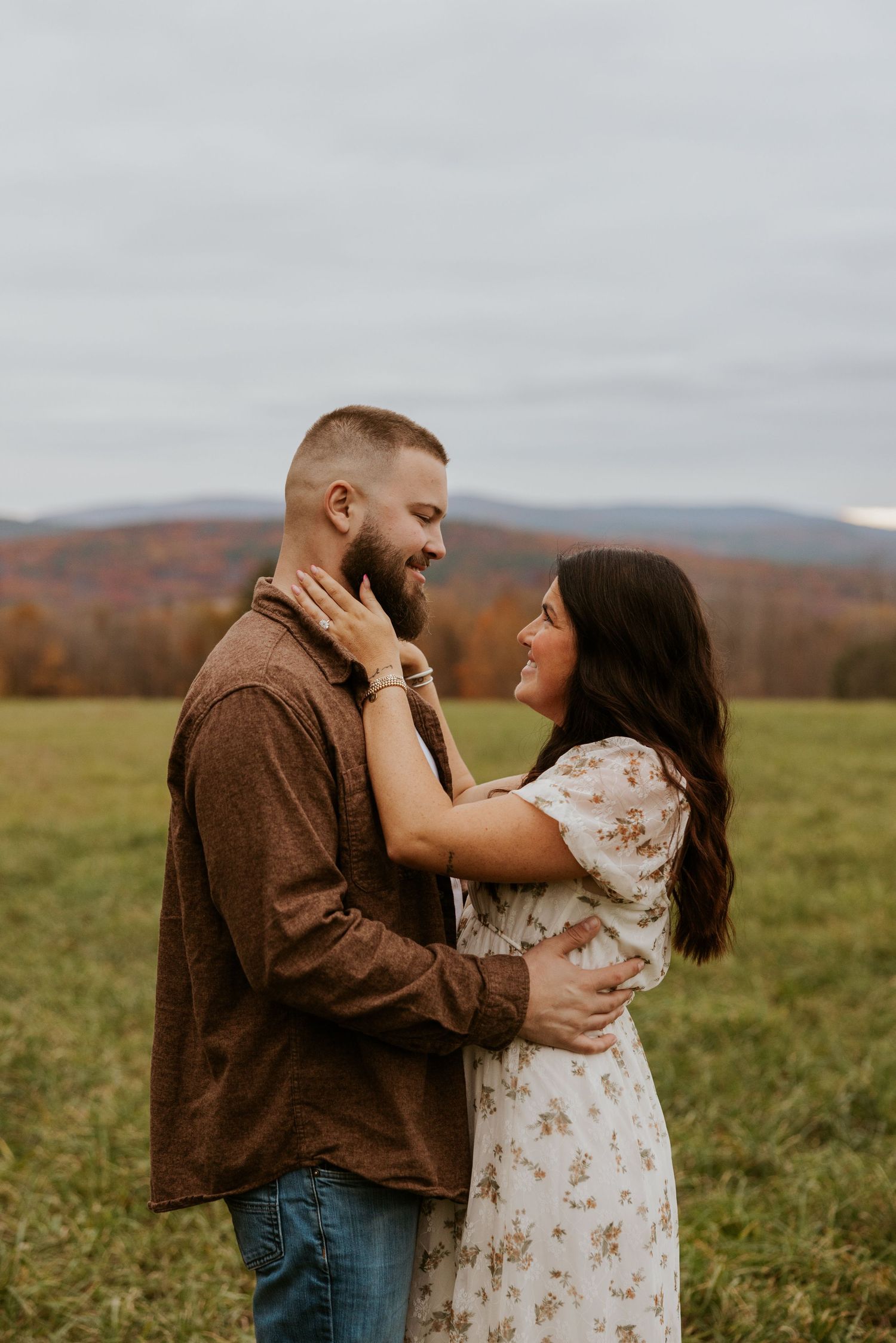 Couple sharing an intimate moment in an autumn field, woman tenderly holding mans face while smiling.