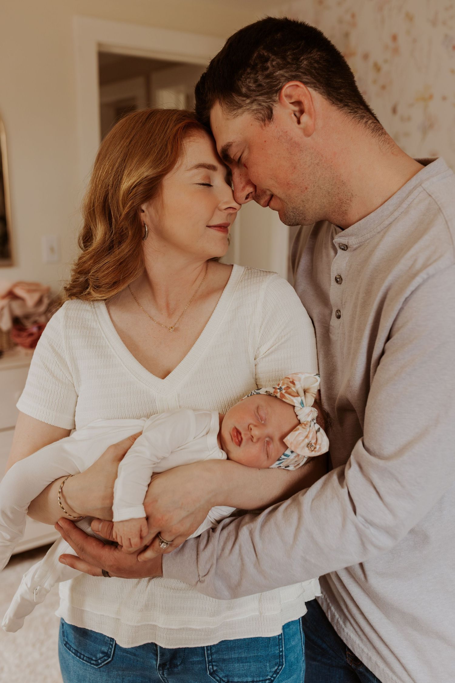 Happy couple touching foreheads while holding their newborn baby girl indoors.