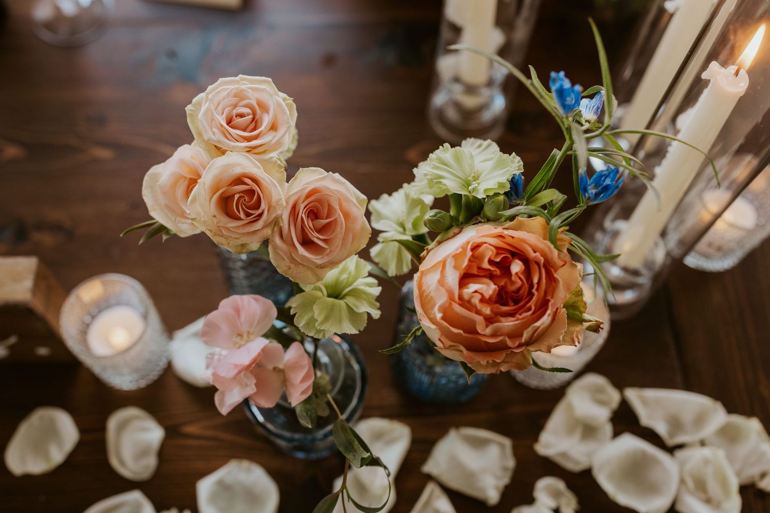 Elegant wedding centerpiece with peach and coral roses in glass vases surrounded by candles.