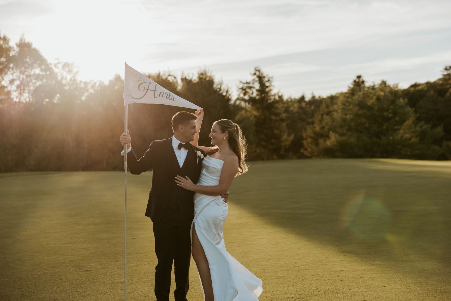 Bride and groom pose with Mr and Mrs pennant flag on golf course at sunset.