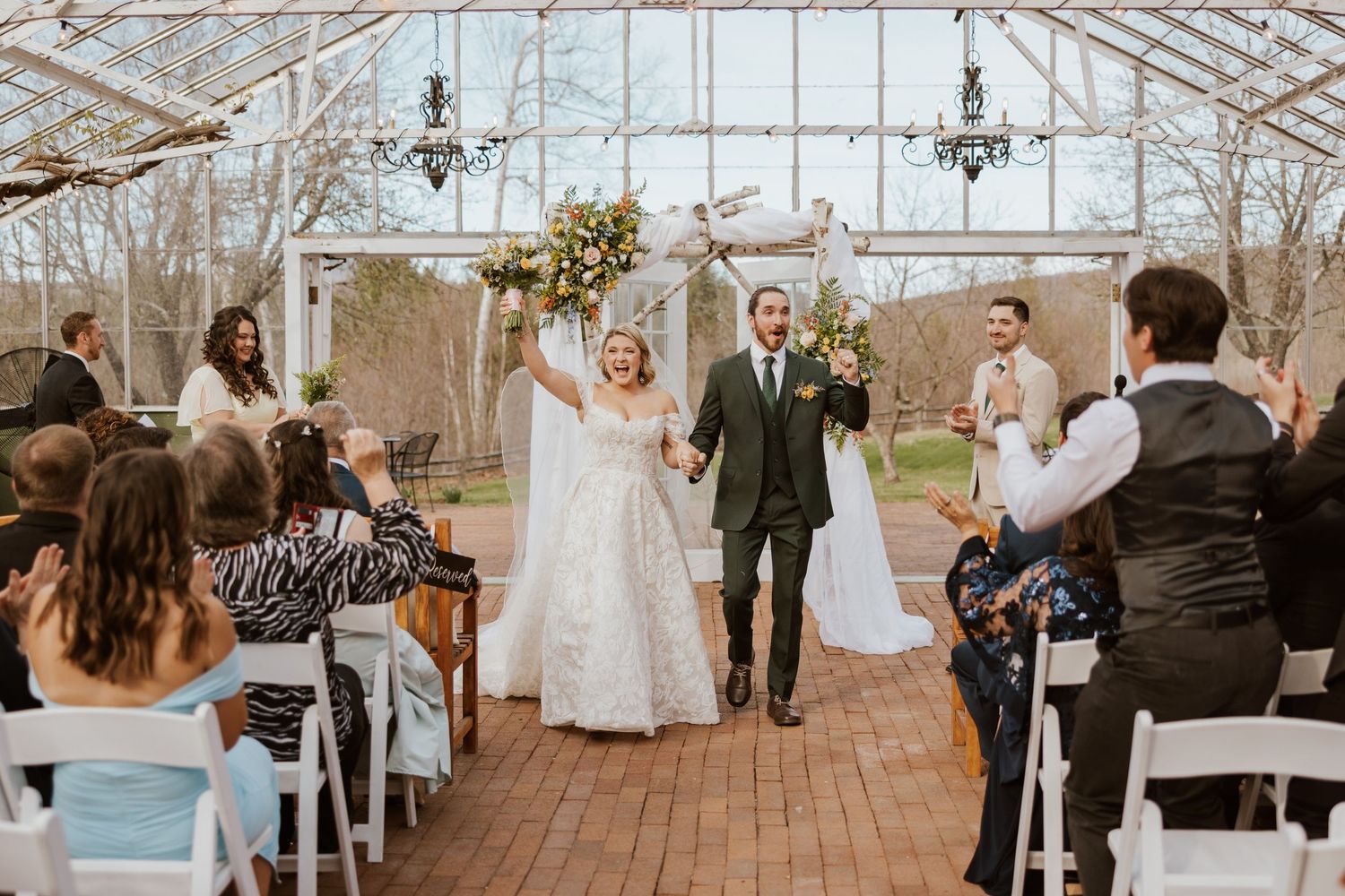 Joyful newlyweds celebrate recessional in a stunning greenhouse wedding venue with guests applauding.