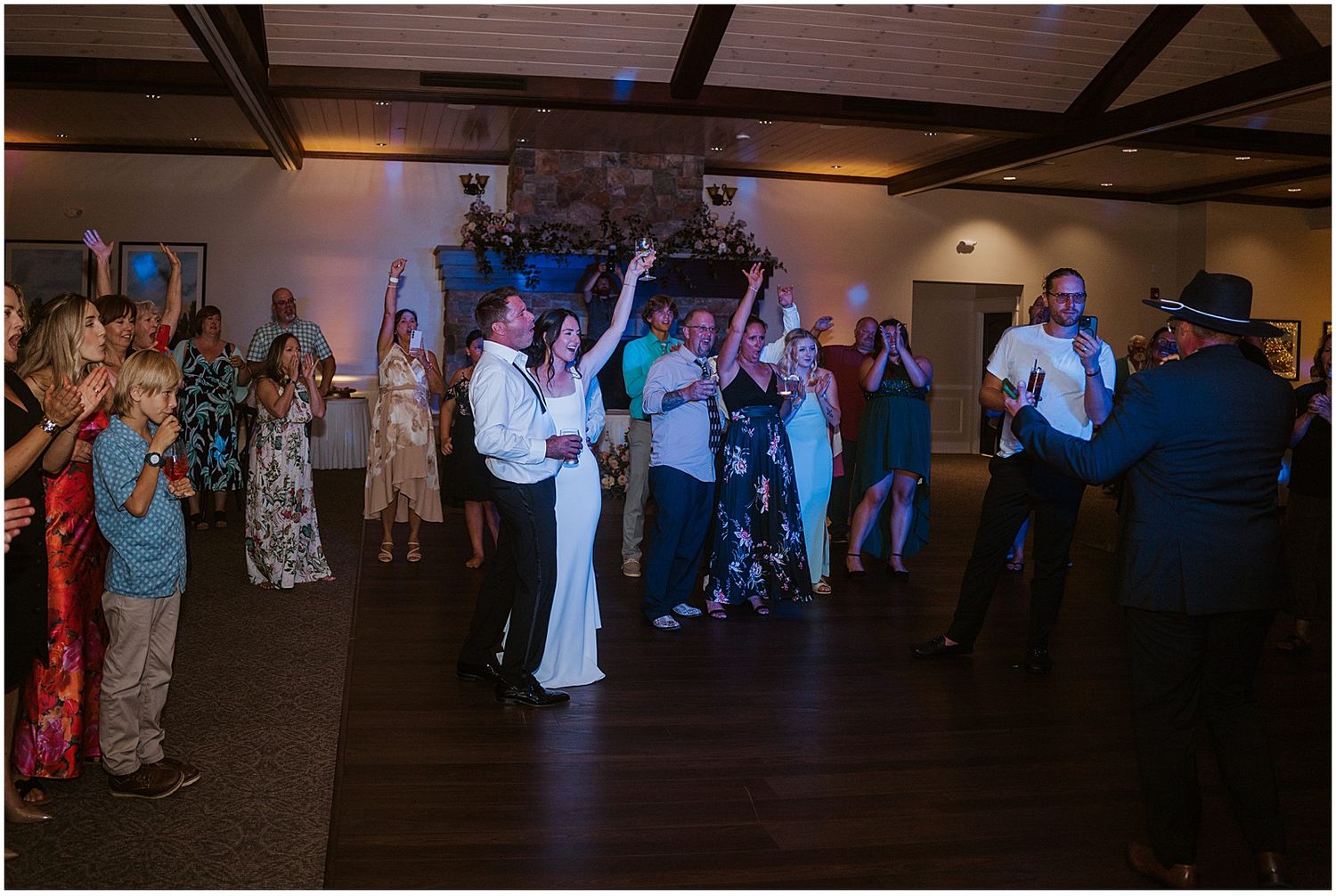 Wedding reception dance floor filled with guests dancing under dim lighting.