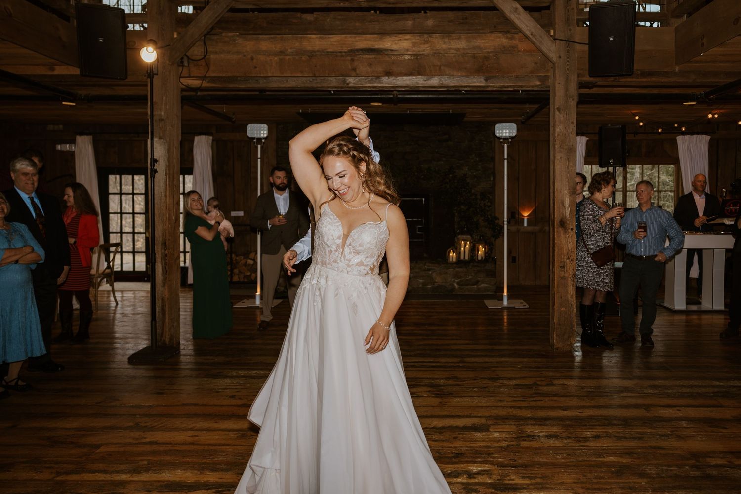 Wedding celebration in a spacious rustic barn venue with exposed wooden beams and warm lighting.