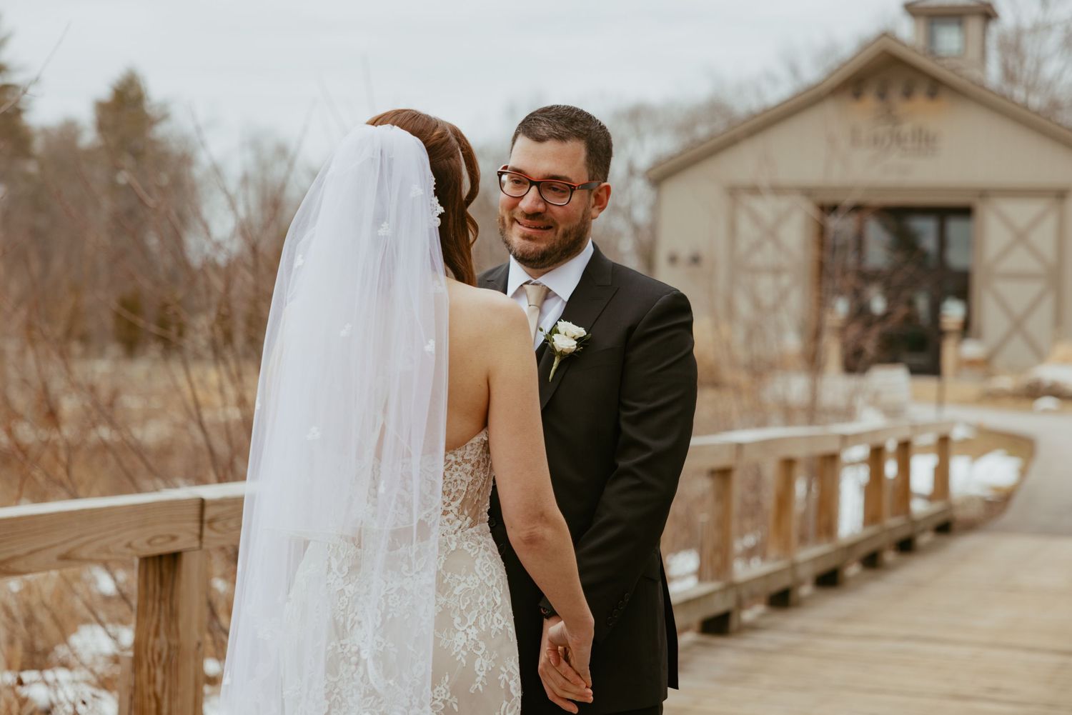 A bride and groom share their first look moment outdoors at a rustic wedding venue.