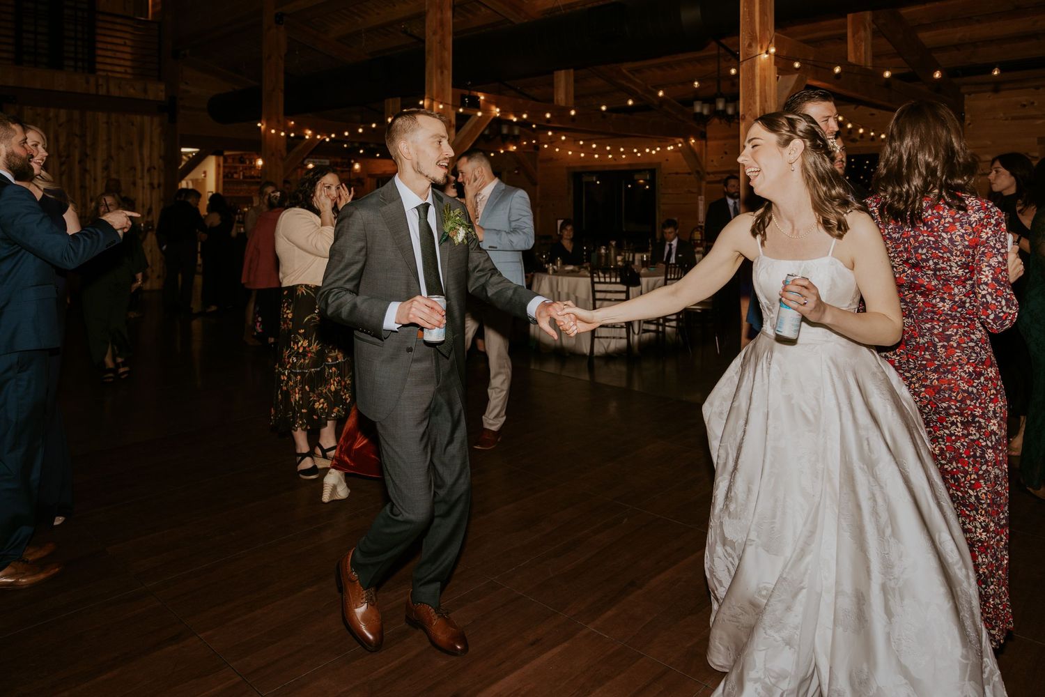 Wedding celebration in a barn venue with string lights and couples dancing on a wooden floor.