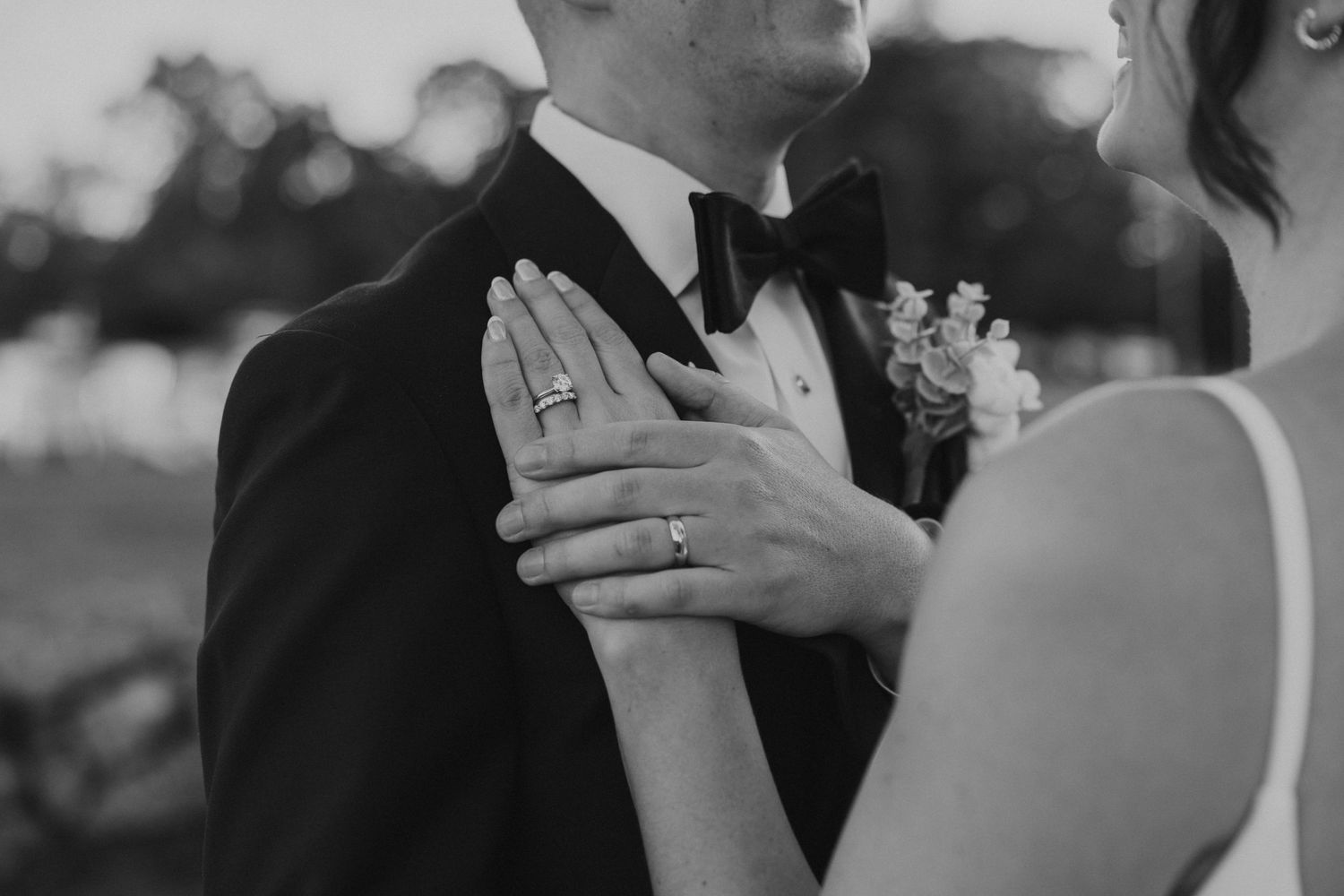 Black and white close-up of bride and groom showing wedding rings on her hand.