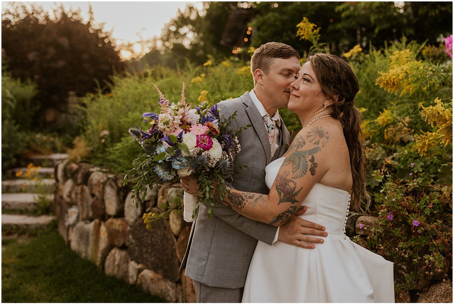 A couple shares an intimate moment in a garden setting with yellow flowers and greenery in the background.