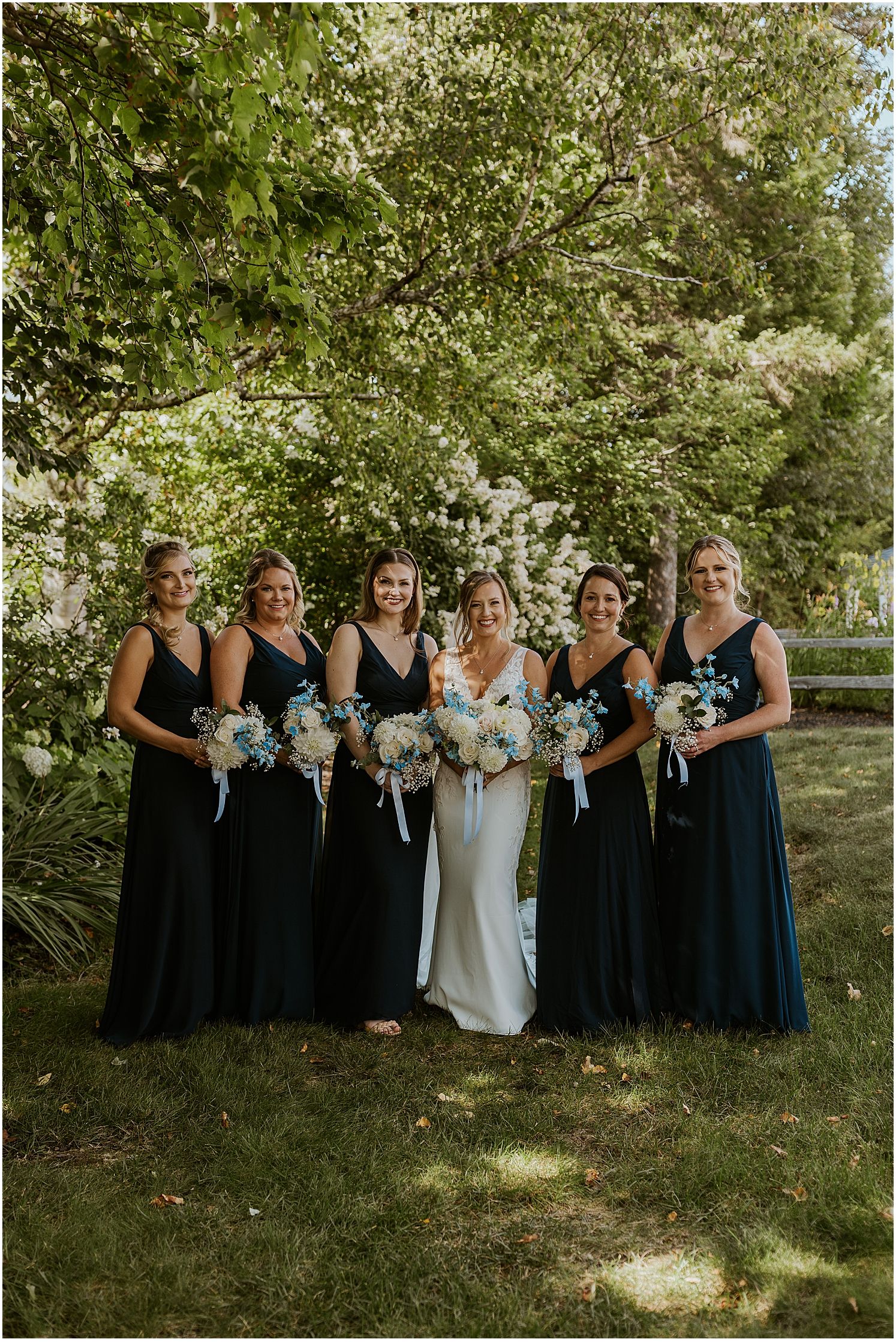 Bridal party in navy blue dresses posing together outdoors with bouquets.