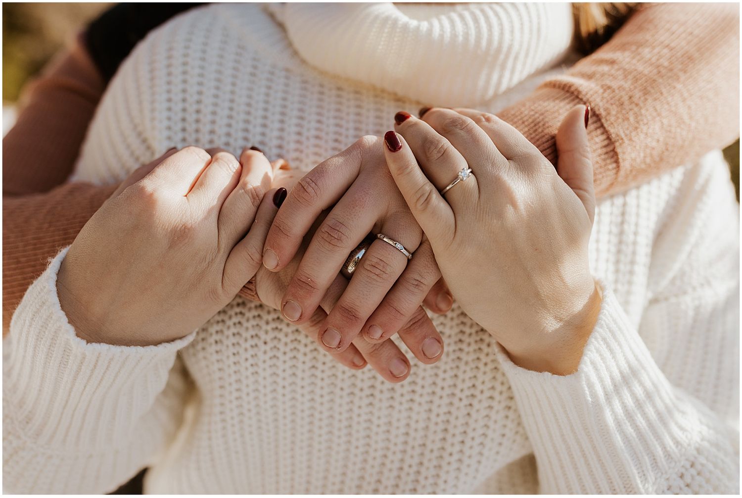 Close-up of hands wearing engagement rings against white knit sweater.