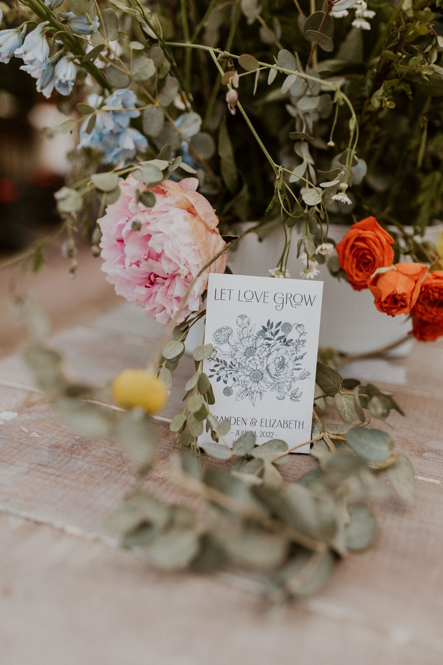 Elegant wedding place cards with floral designs displayed among pink and orange roses on a textured tablecloth.