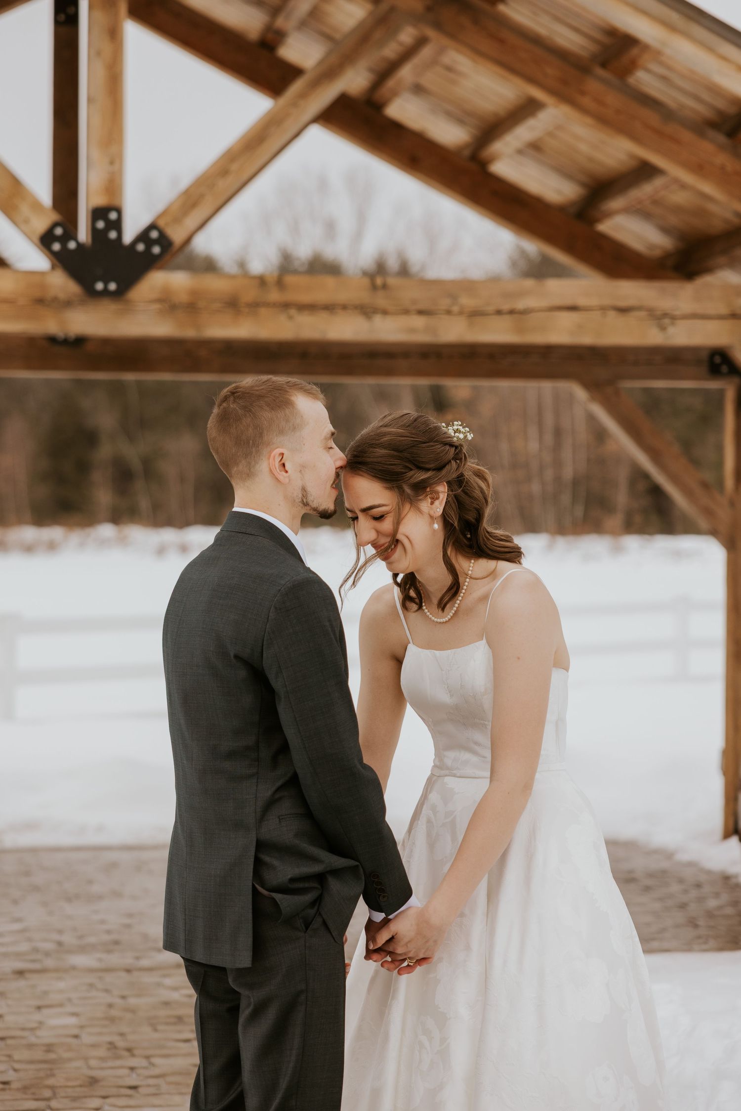 A romantic wedding moment captured under a wooden pavilion in a snowy winter setting.