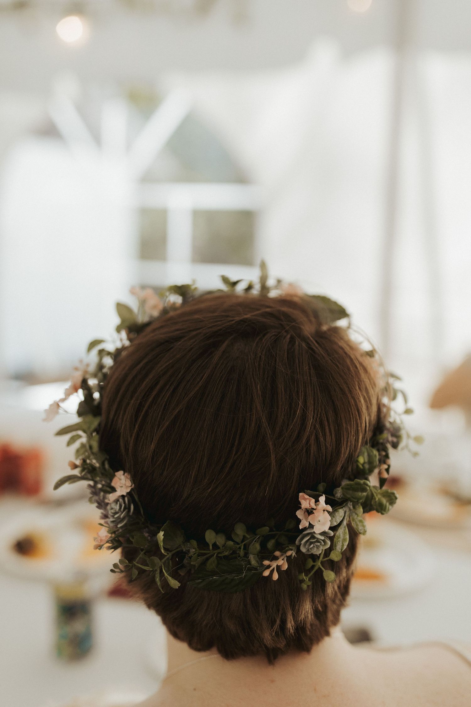 Close-up of delicate floral crown with greenery and small flowers on dark hair.