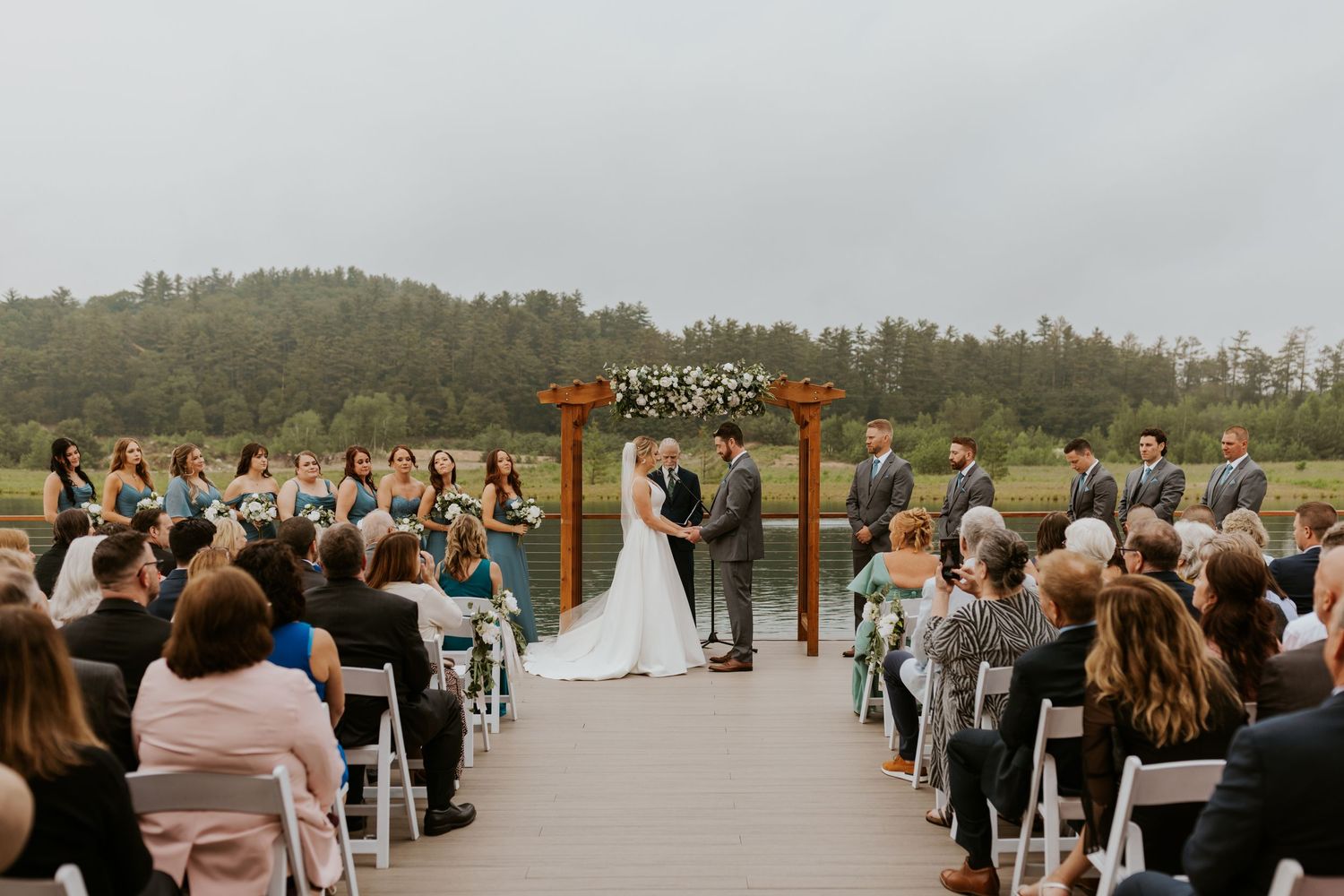Outdoor wedding ceremony with bride and groom at altar overlooking a scenic landscape.