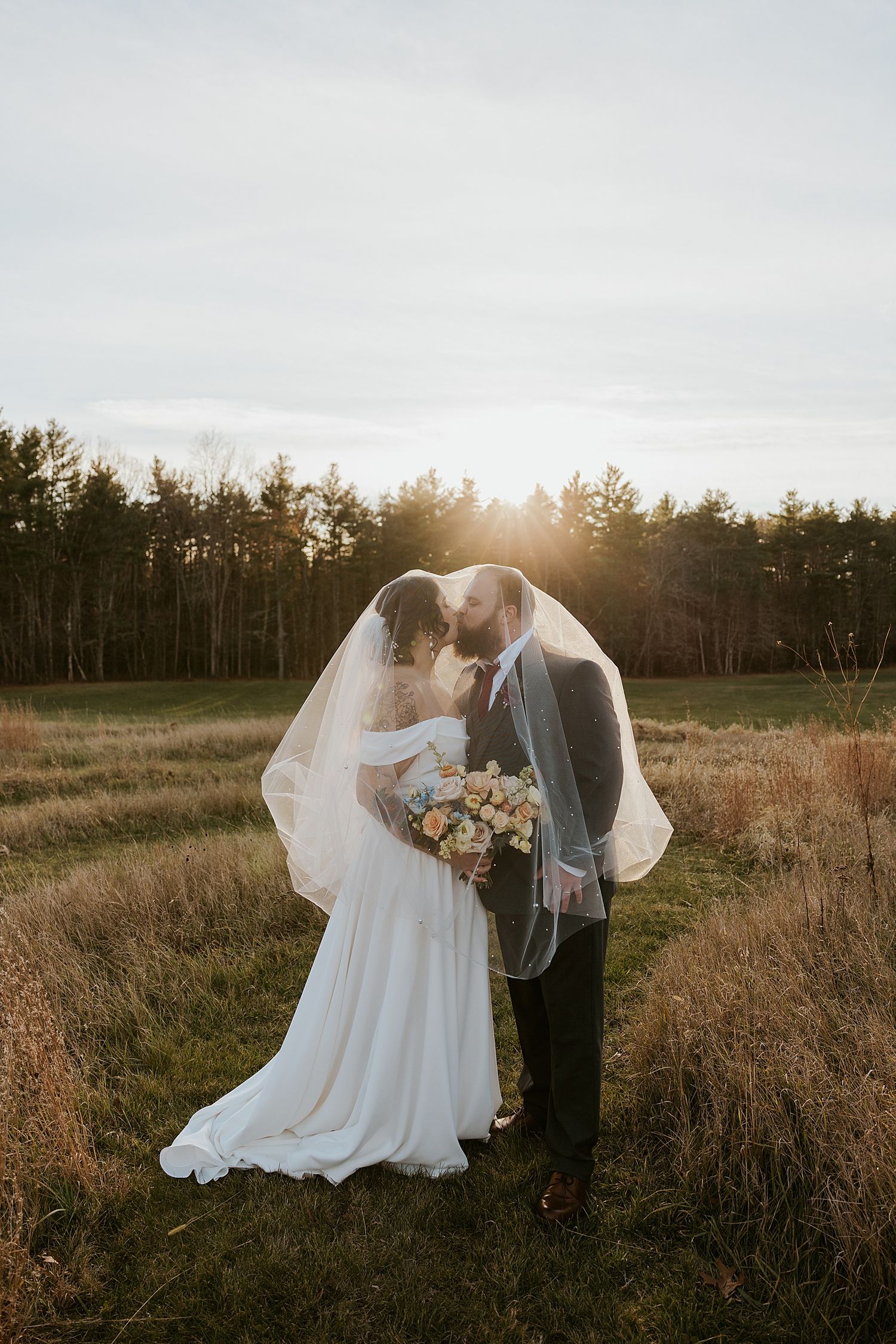 Couple taking sunset portraits under the bride's veil at their NH wedding
