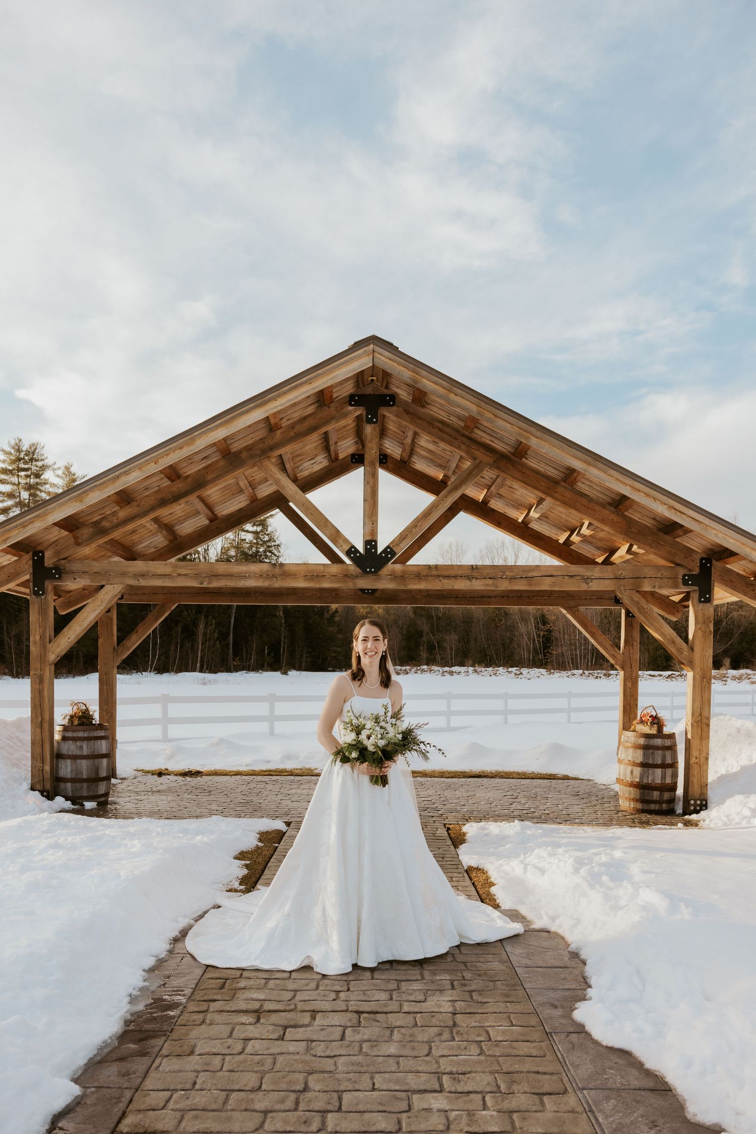 A winter wedding scene showing a wooden pavilion with snowy surroundings and a white dress against a cloudy sky.