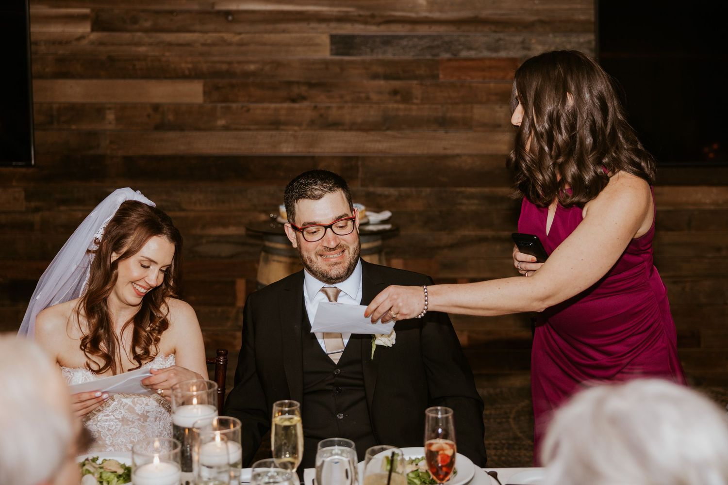 Wedding reception table setting with rustic wood wall backdrop and decorative centerpieces.