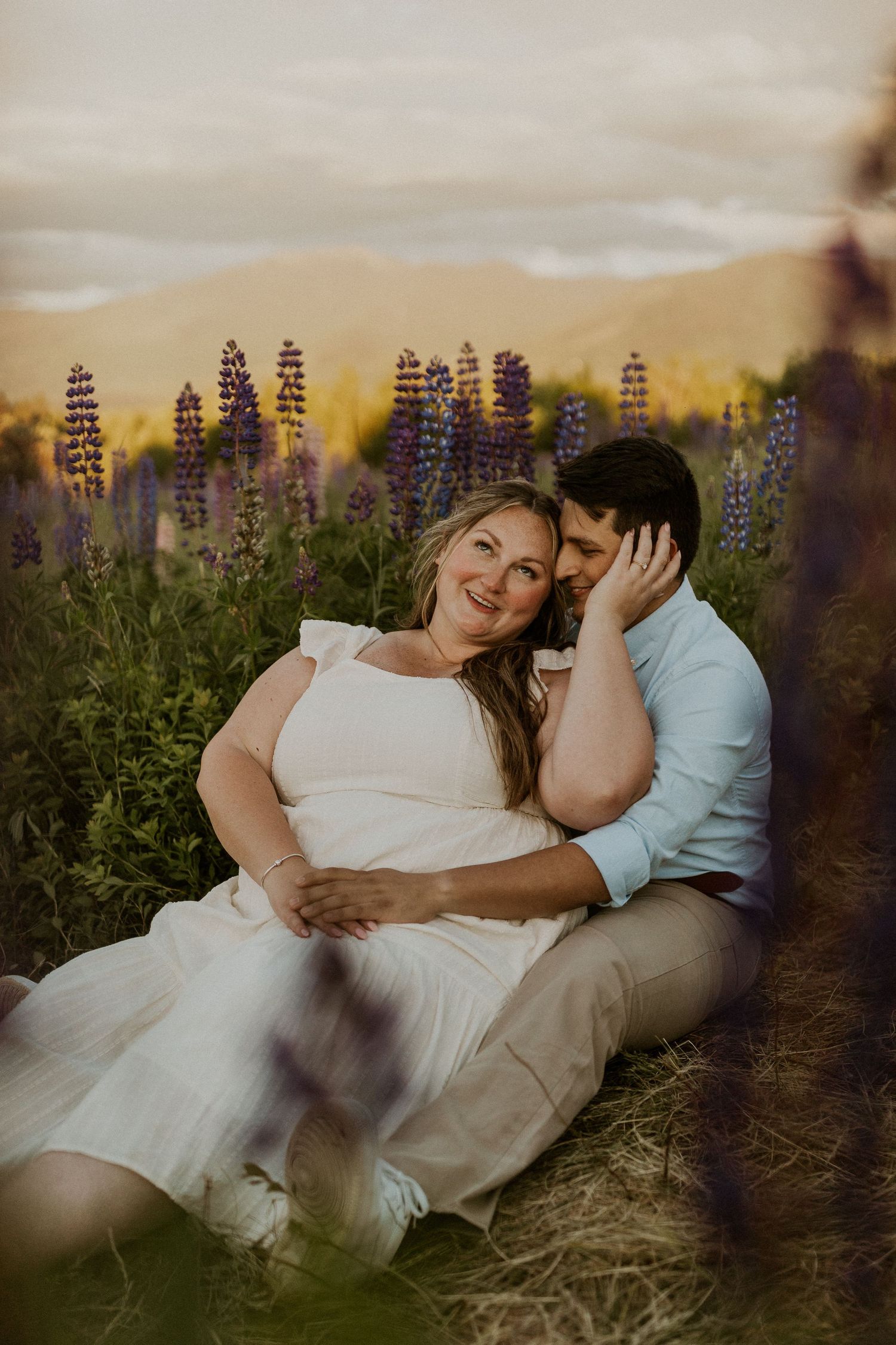 Terise and Jose cuddling up together in a field of purple lupines in Sugar Hill New Hampshire.