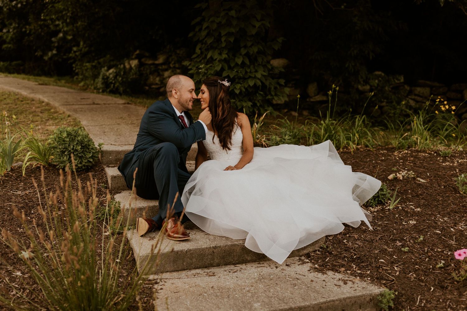 Wedding couple poses outdoors against natural foliage backdrop.