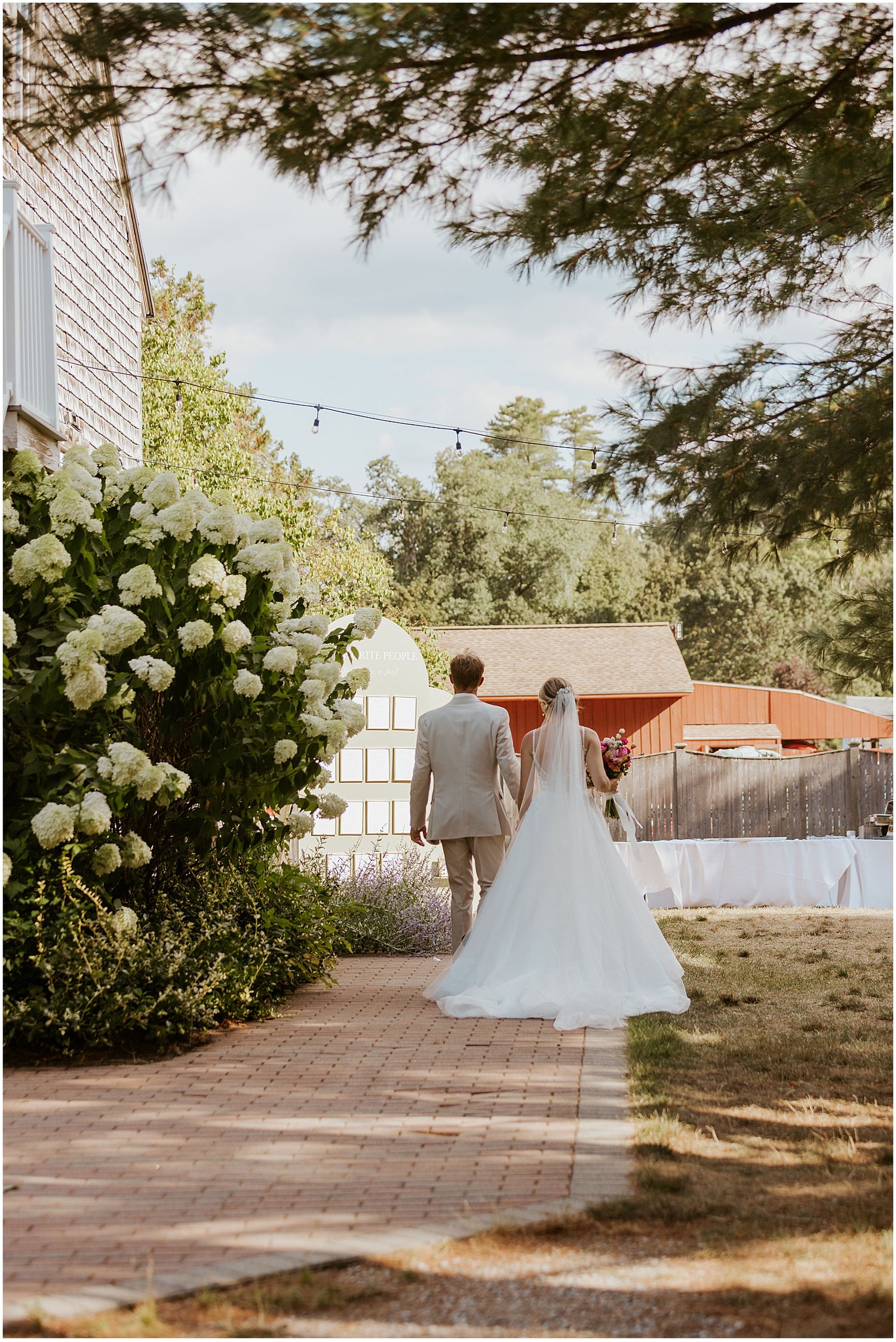 Wedding ceremony setup on a brick pathway with white chairs and floral arrangements.