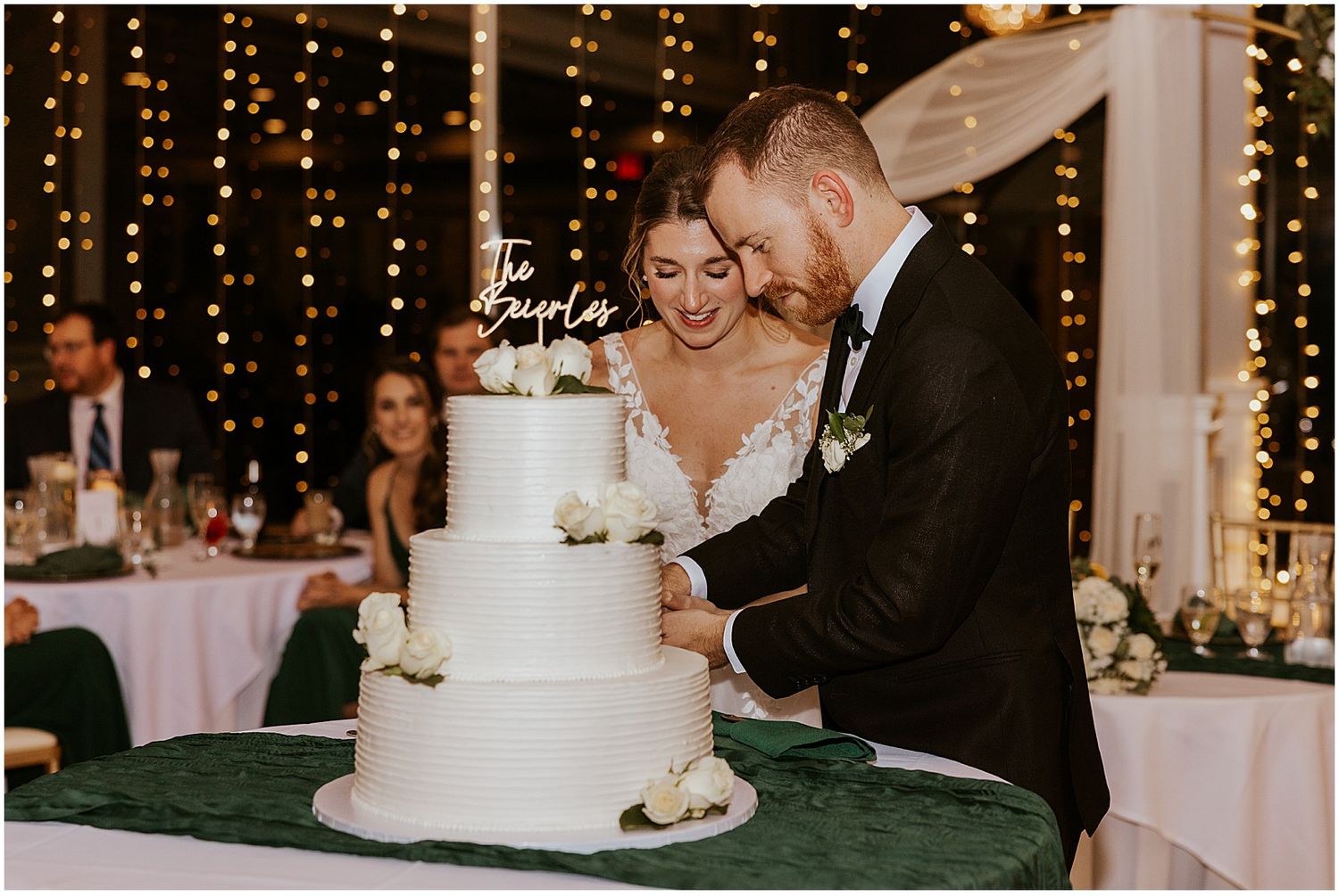 Wedding reception venue decorated with string lights and a white tiered cake on display.