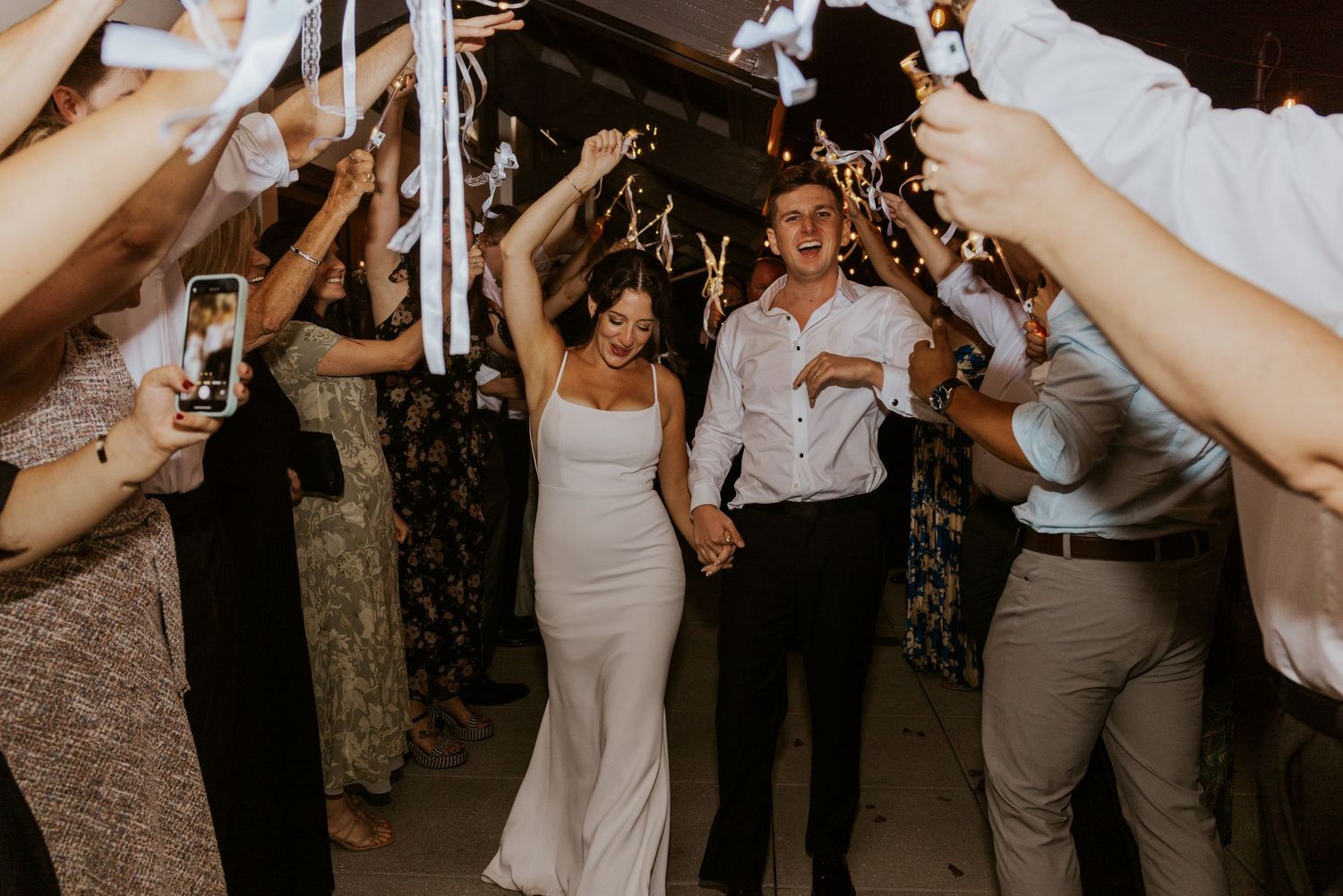 Bride and groom walk through sparkler exit tunnel surrounded by cheering wedding guests at night.