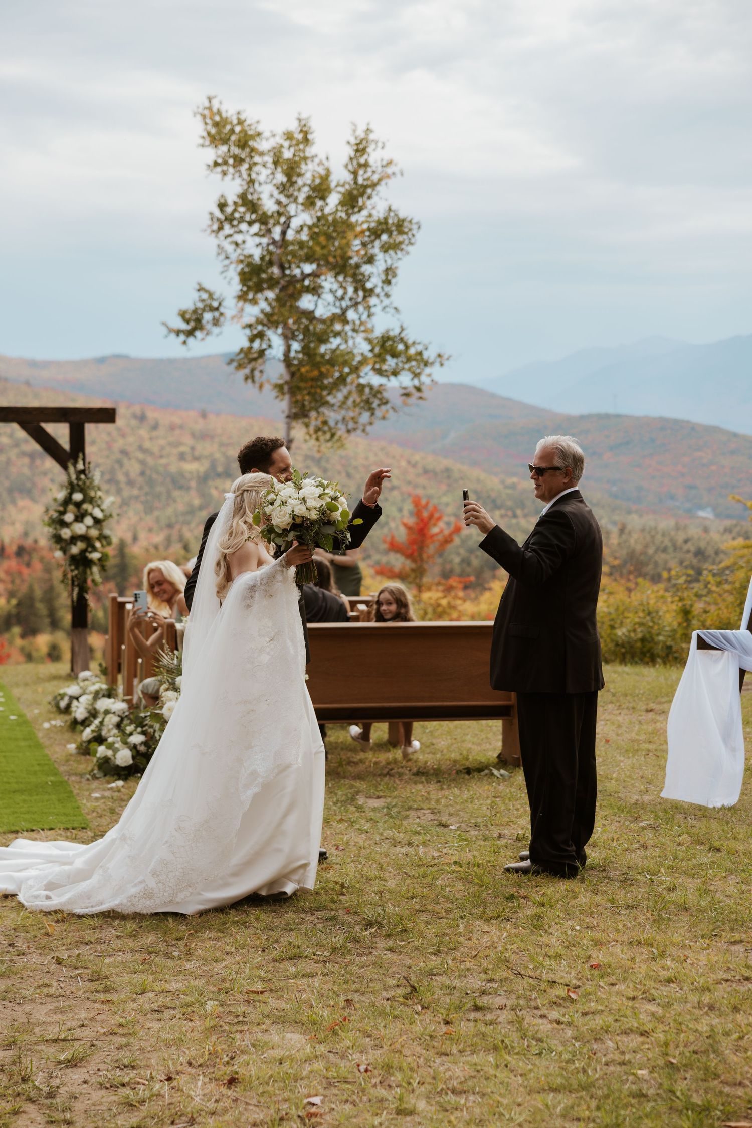 Bride and groom toast at outdoor fall mountain wedding ceremony with colorful foliage backdrop.