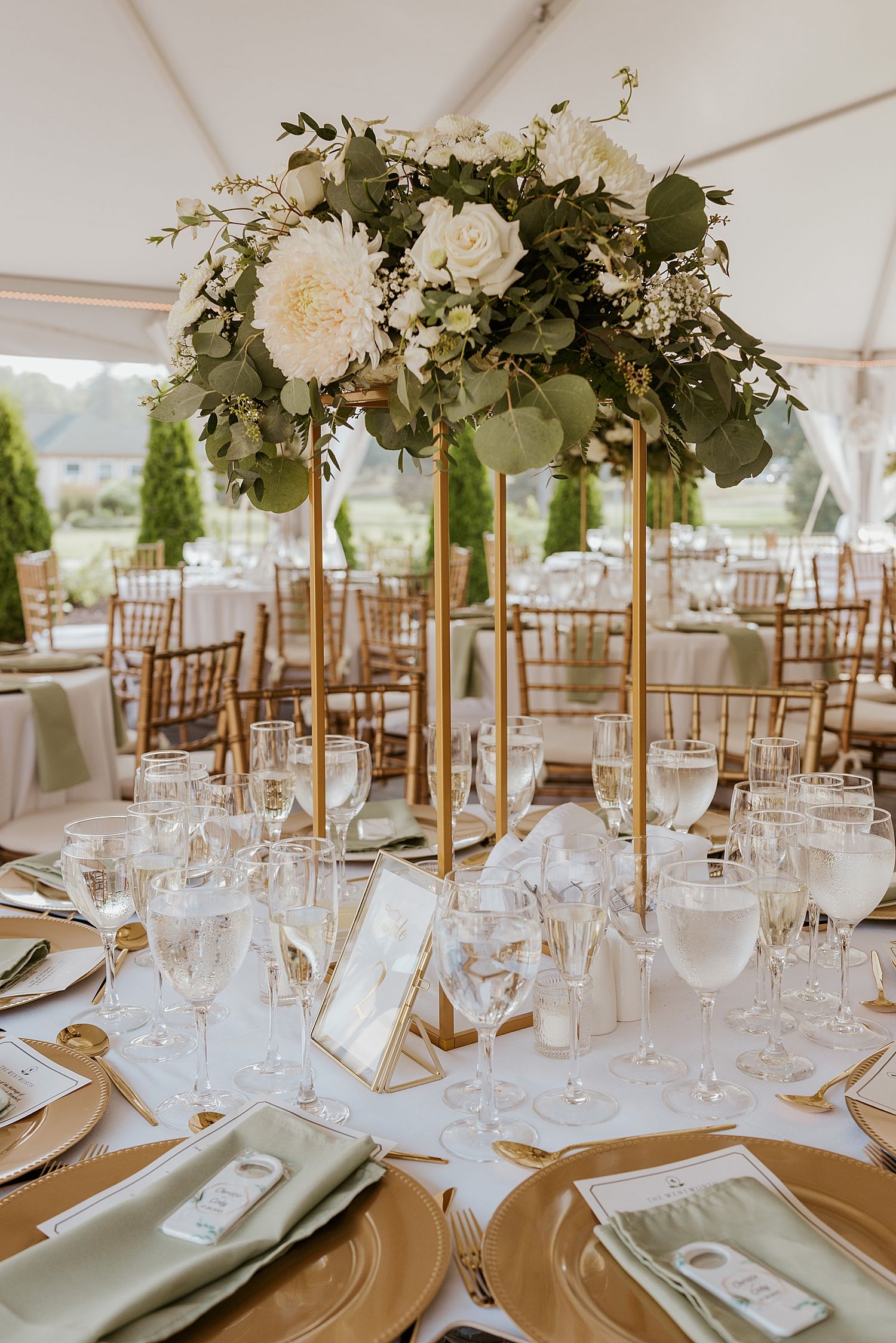Elegant wedding reception table with tall gold centerpiece featuring white roses, dahlias, and eucalyptus greenery for a NH wedding