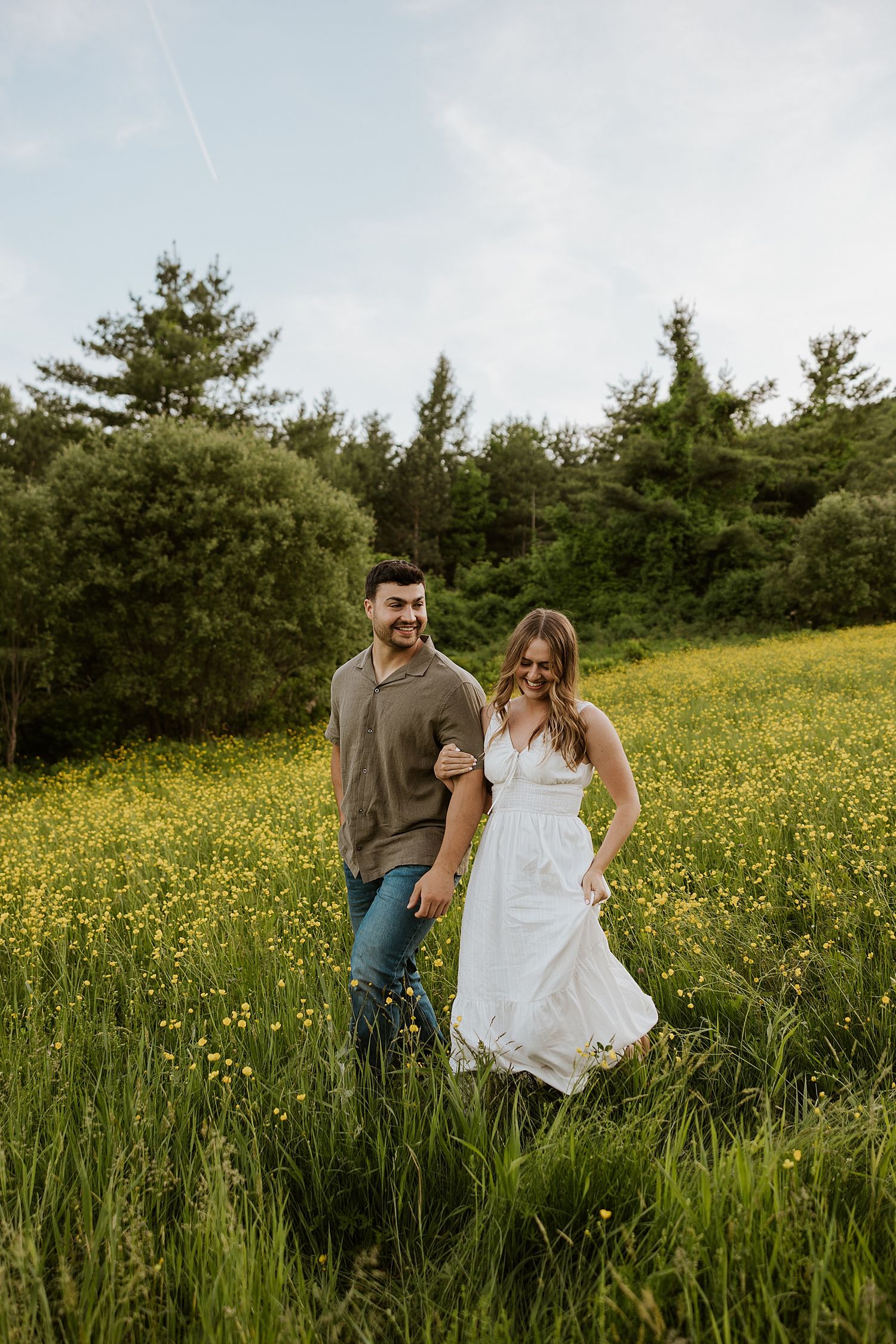 Couple walking through a wildflower field taking golden hour engagement photos in NH